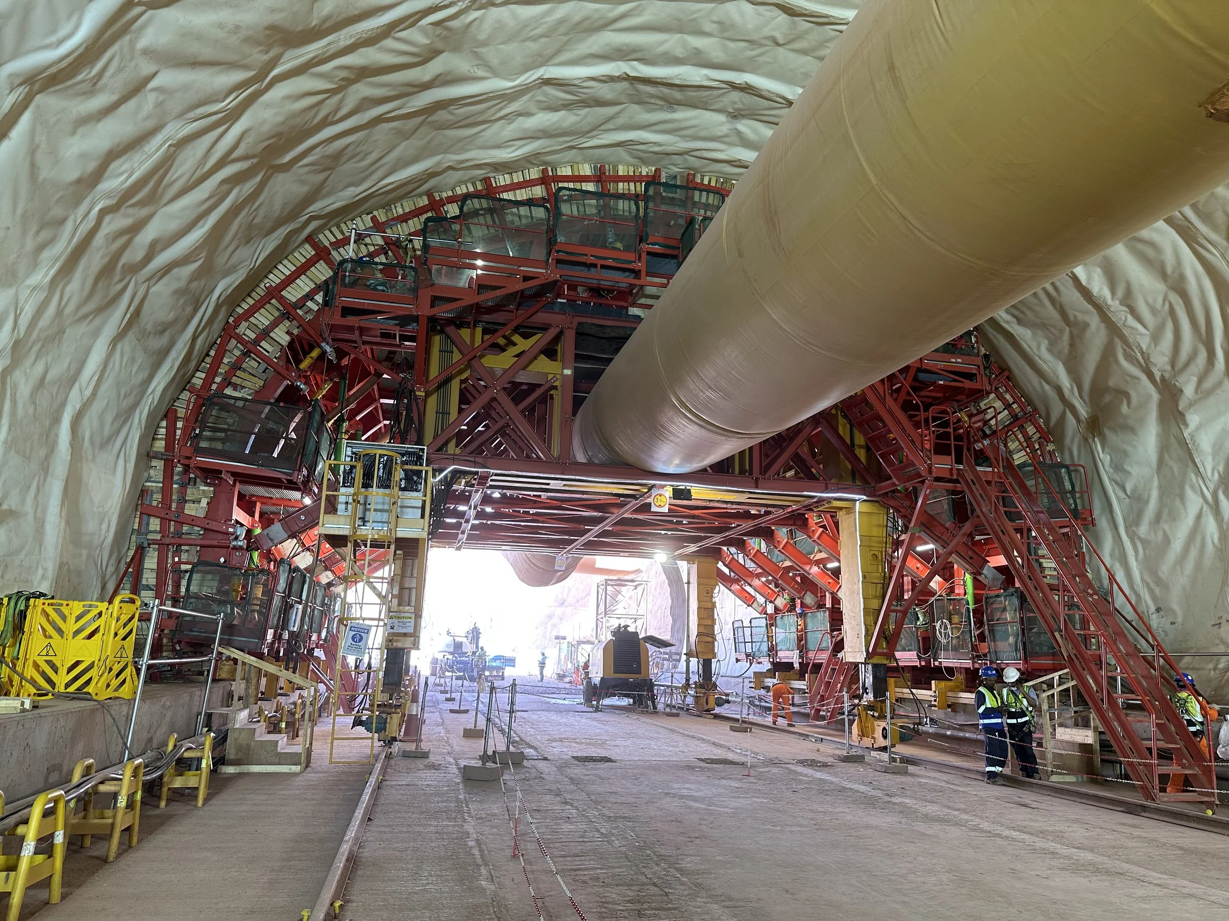 Construction workers inside a tunnel with large machinery and safety barriers.