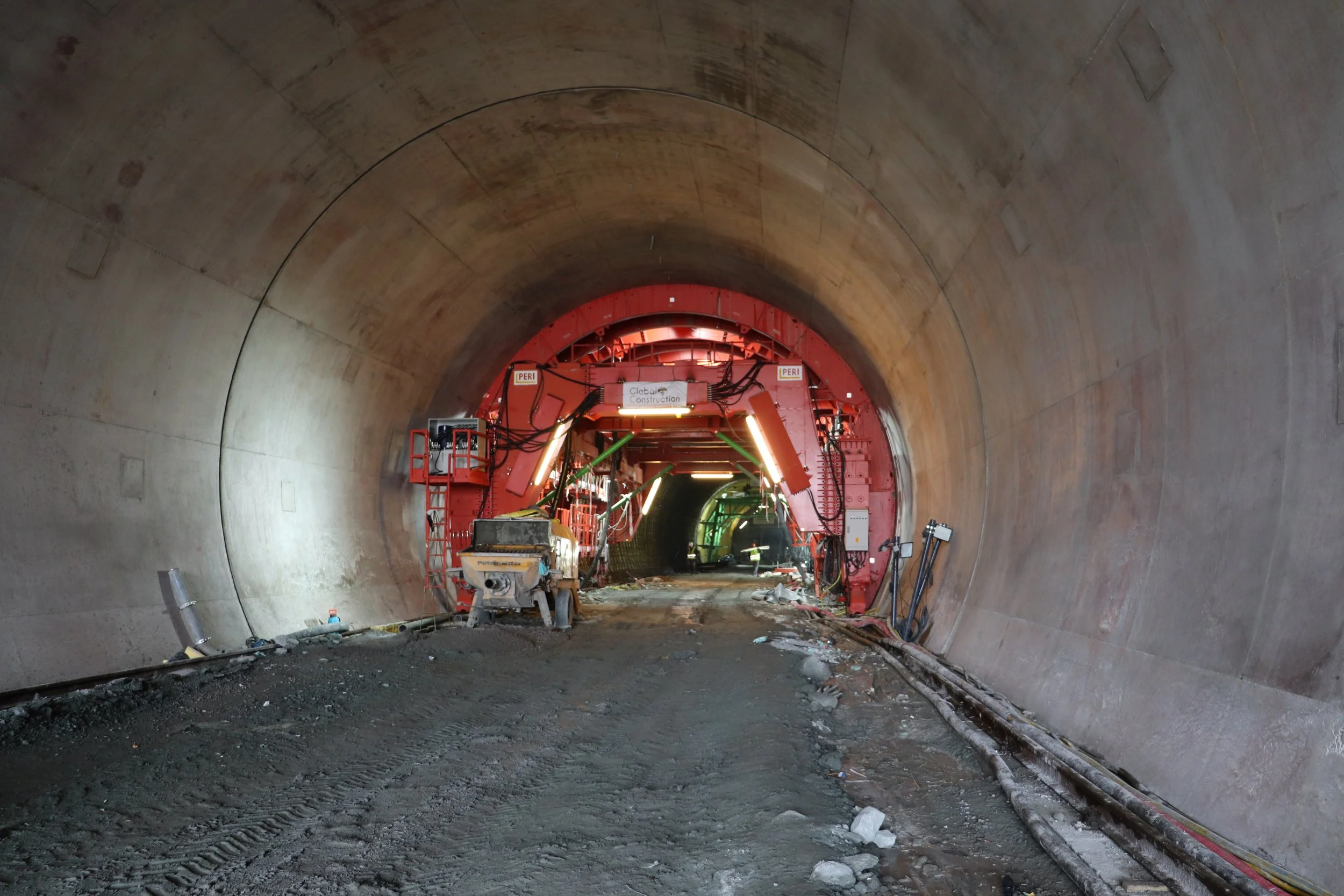 Construction inside a tunnel with construction equipment, dirt floor, and illuminated lights.