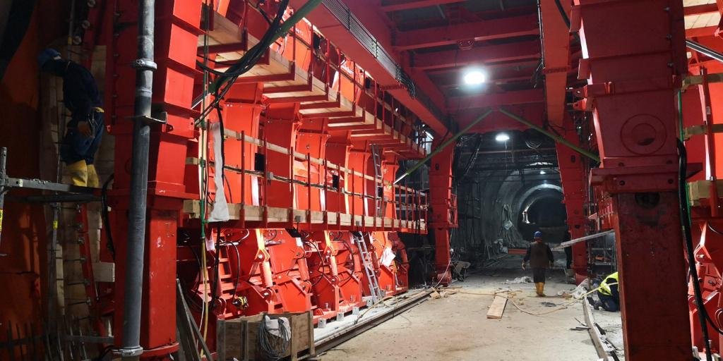 Underground tunnel construction site with red support structures and workers.