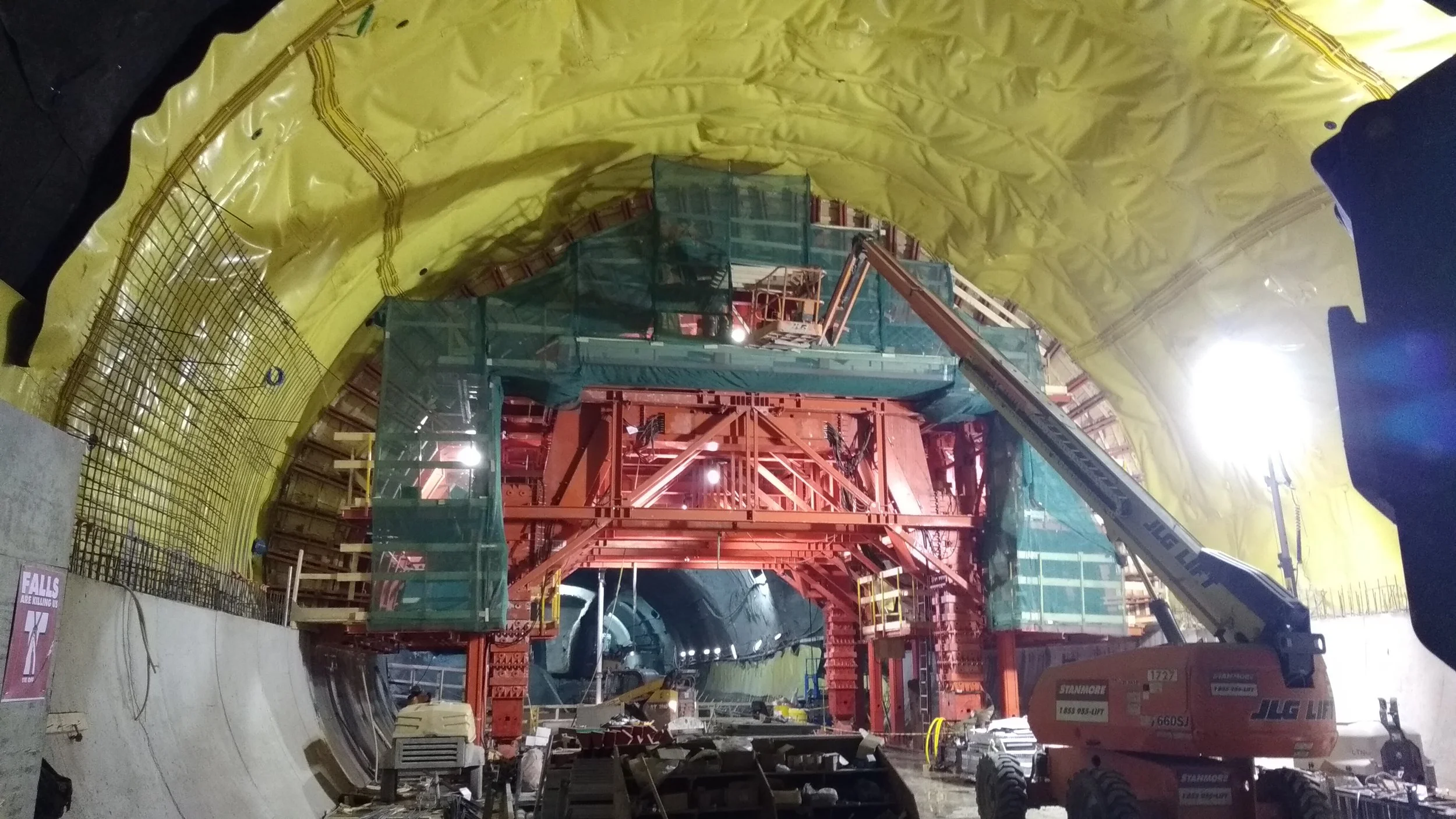 Construction inside a large tunnel with machinery, scaffolding, and protective yellow and green barriers.
