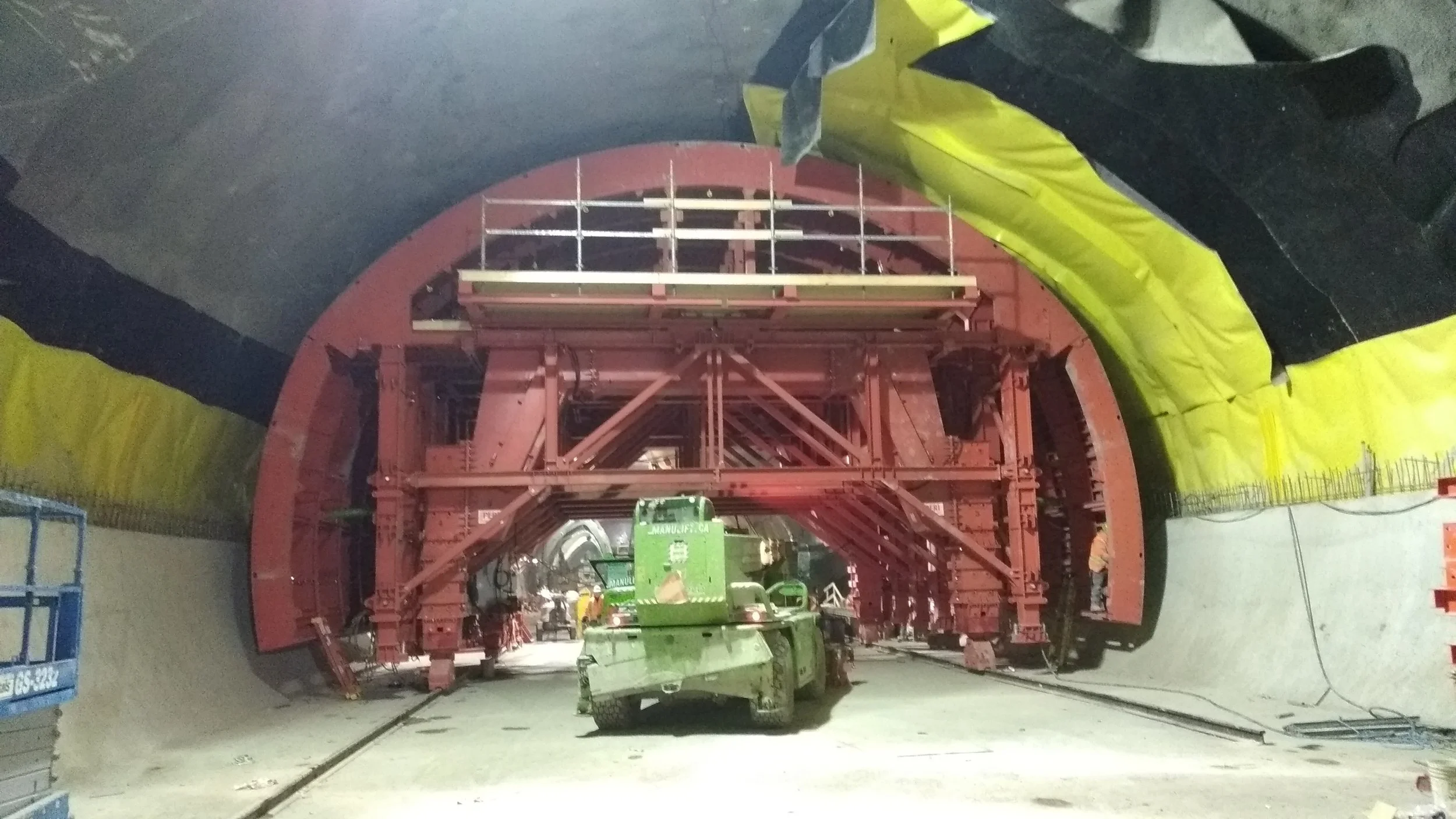 Construction workers inside a tunnel with a large red tunnel boring machine and construction equipment.