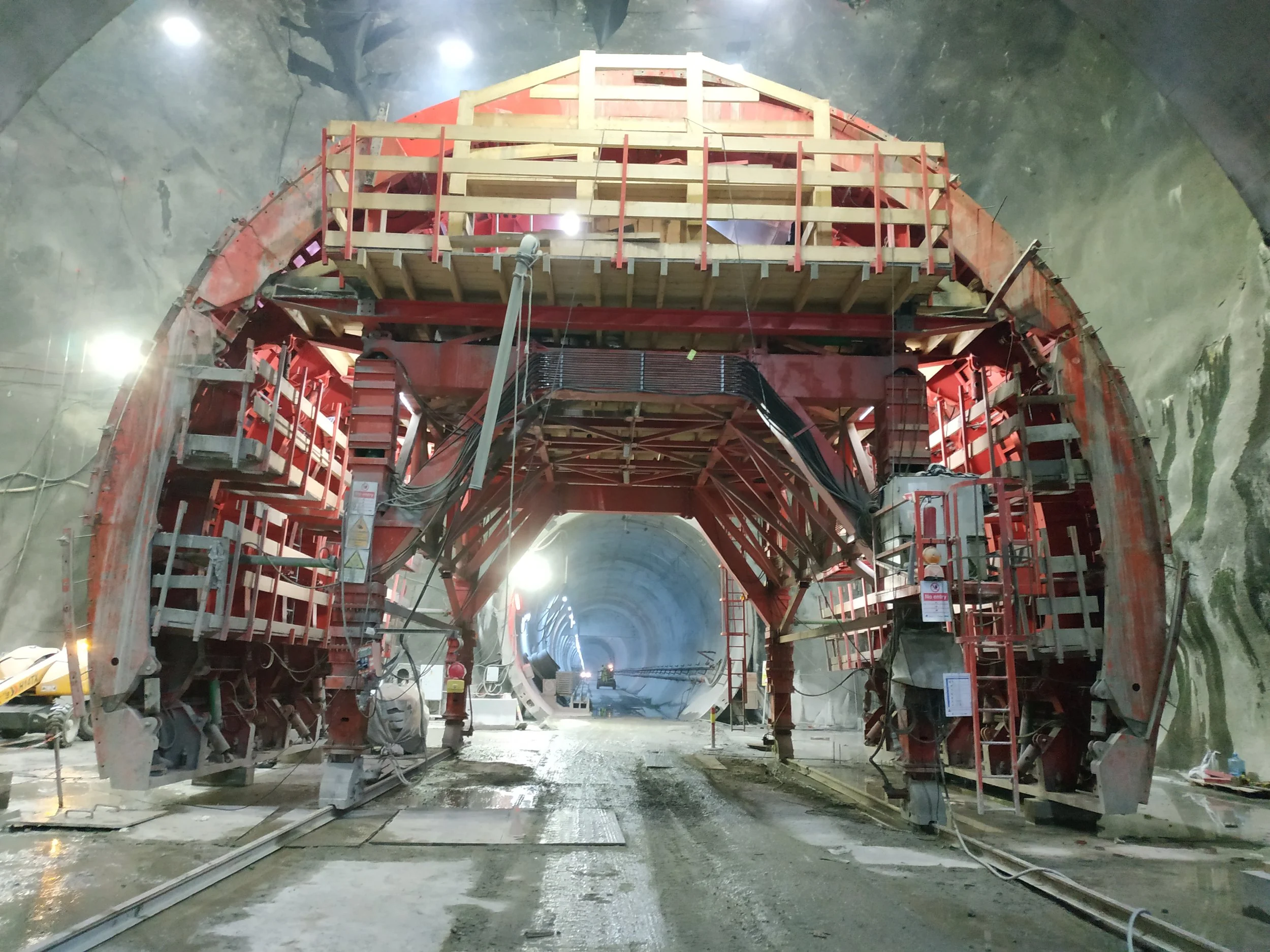 Construction inside a large tunnel with machinery, scaffolding, and safety equipment.