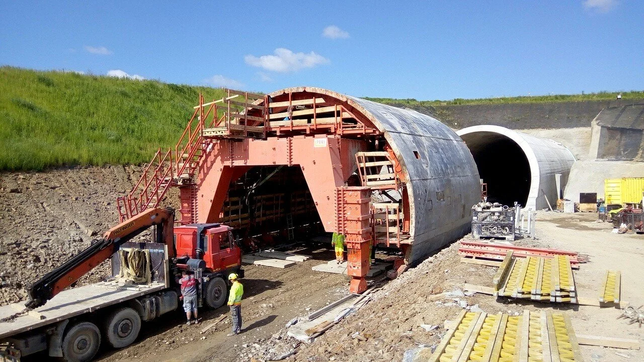 Construction workers building a tunnel with a large, partially completed tunnel structure and a tunnel entrance in the background.