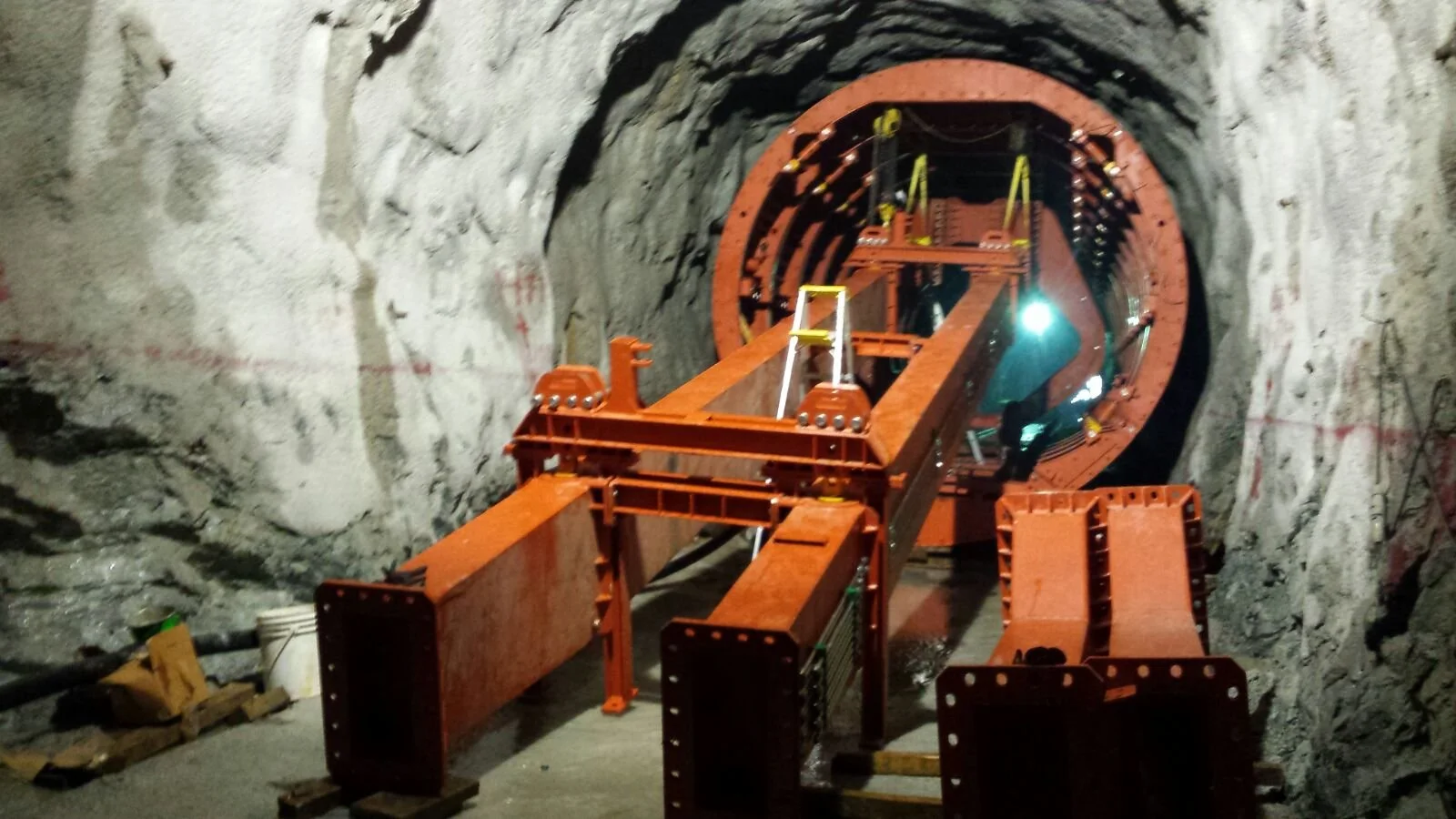 Construction of a tunnel with orange support structures and machinery in an underground rock excavation site.