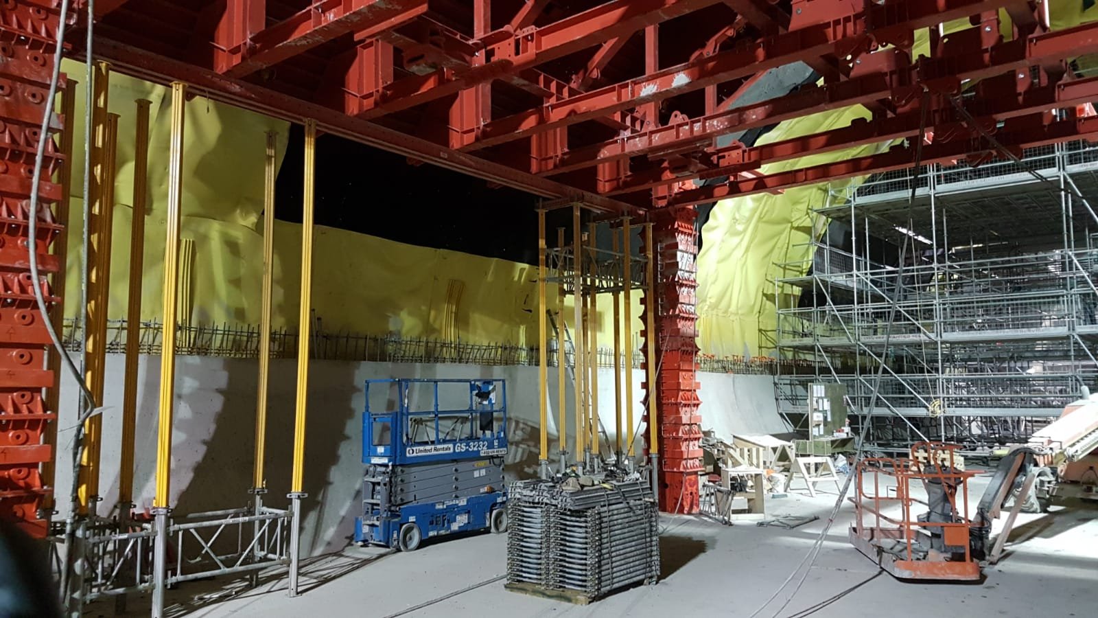 Construction site with scaffolding, red structural elements, and yellow insulation or sheathing, at night.