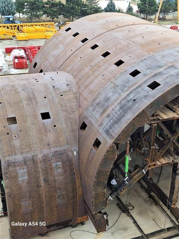 Close-up of large curved metal structures under construction, with multiple square and rectangular openings, located outdoors with tools and machinery around.