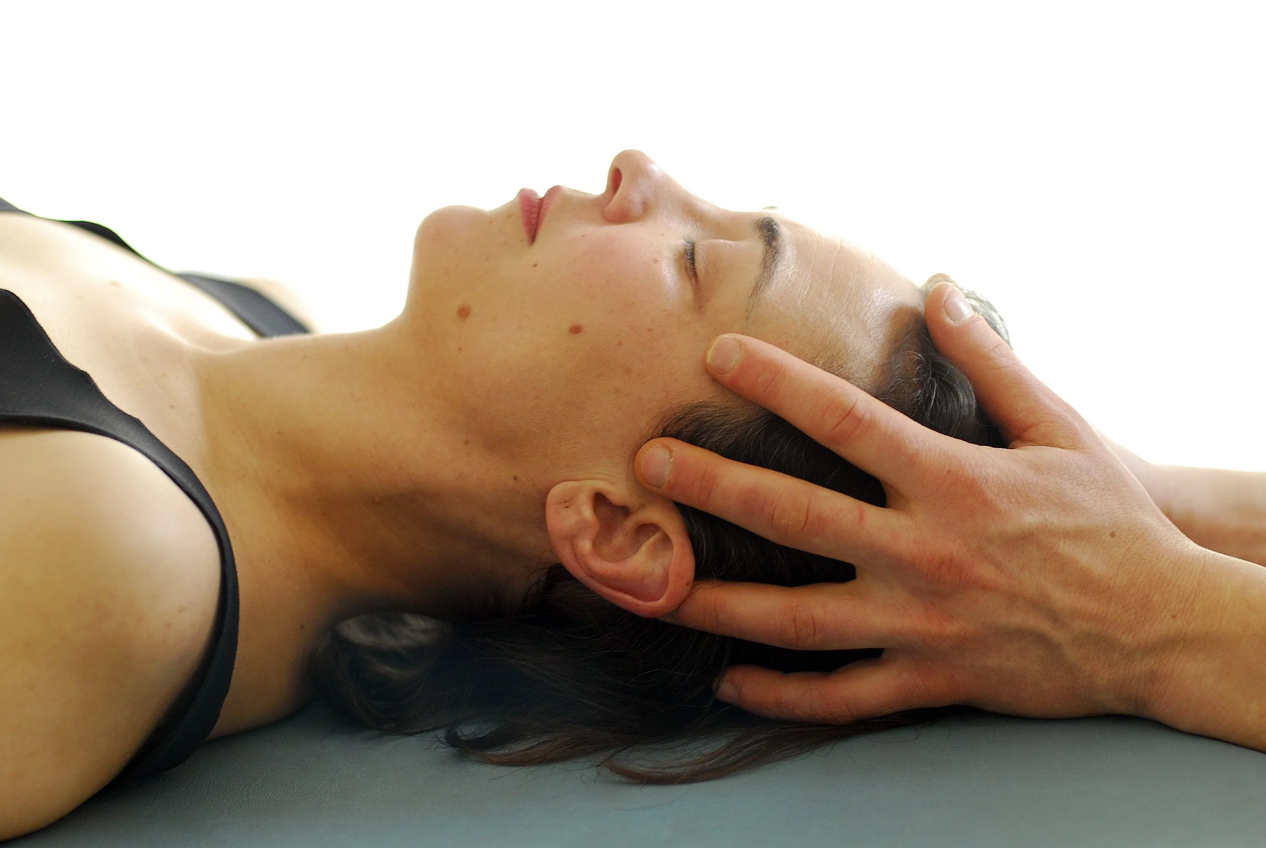 Frau erhält eine entspannende Massage am Kopf, liegend auf einer Matte.