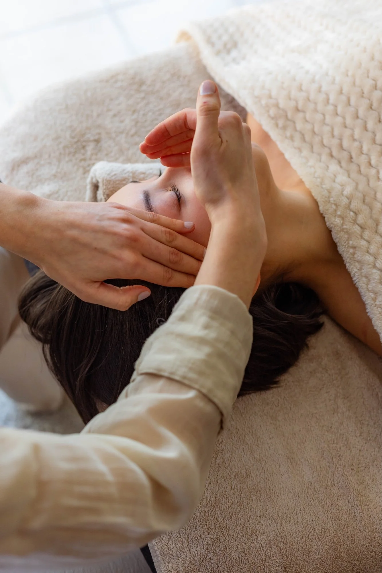 Une femme reçoit un massage facial dans un endroit confortable avec une couverture beige.