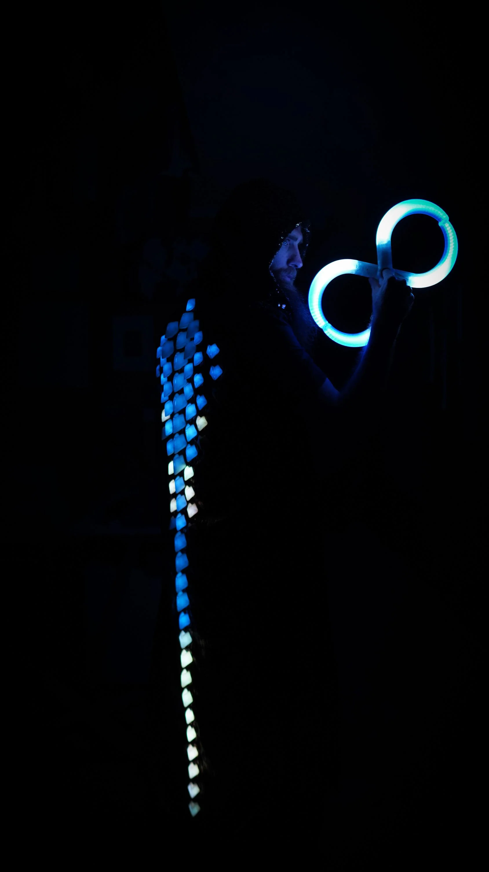 Flow artist performing with Alpha Kilo Victor Finger Buugeng LED flow toys creating a blue infinity light pattern