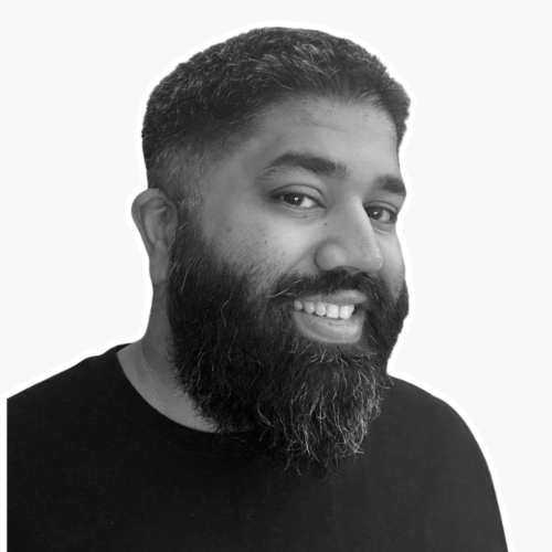 A smiling man with a full beard and short hair, wearing a black shirt, looking at the camera against a white background.