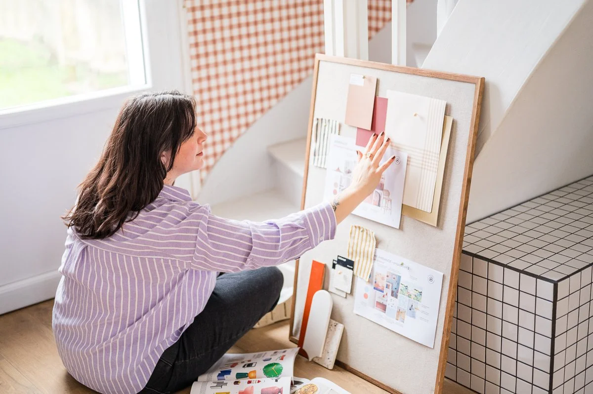 Une femme regarde un tableau d'affichage avec des échantillons de matériaux, de couleurs et d'idées de décoration à l'intérieur.
