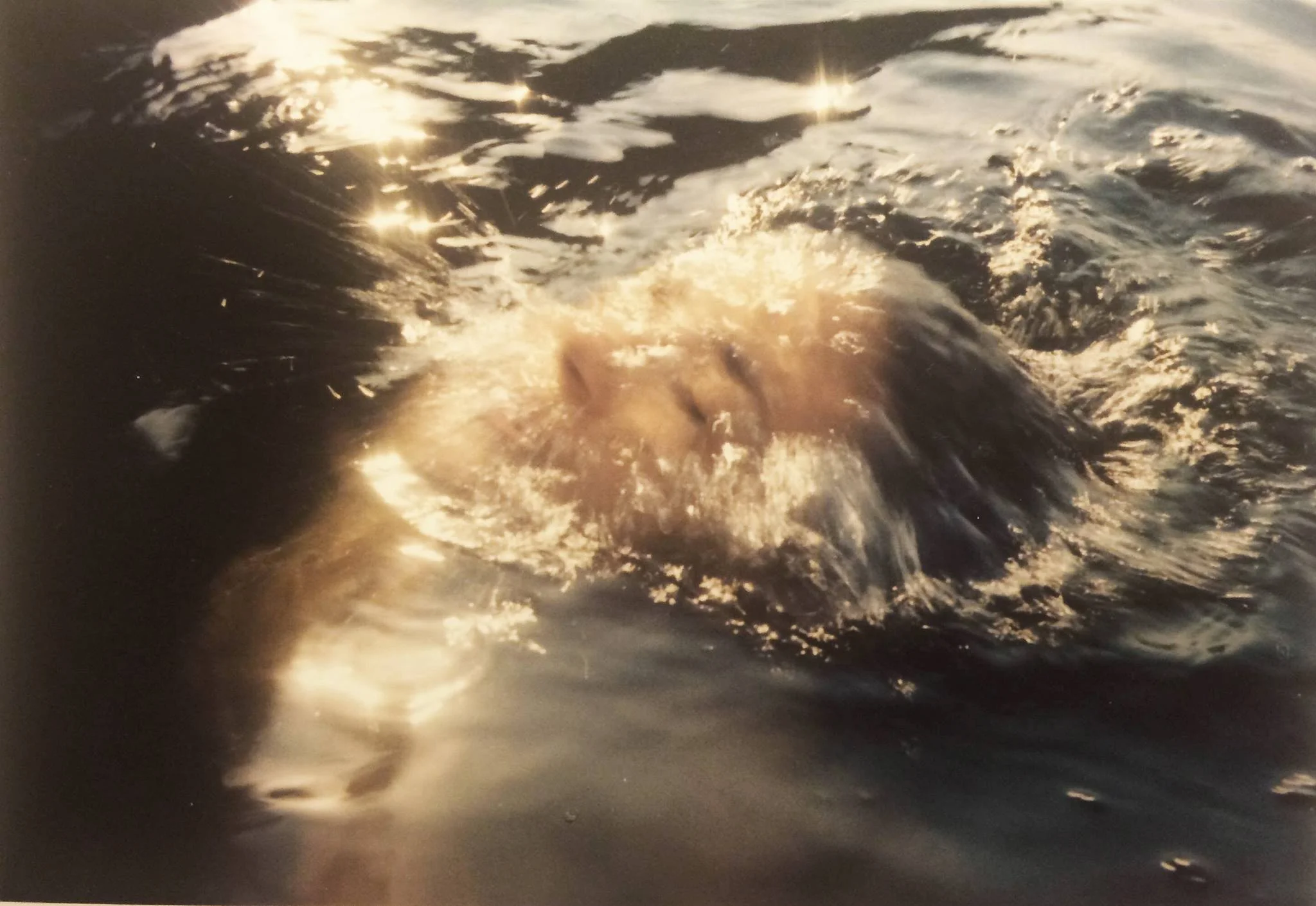 A person swimming underwater in the ocean at sunset, with sunlight reflecting off the water.