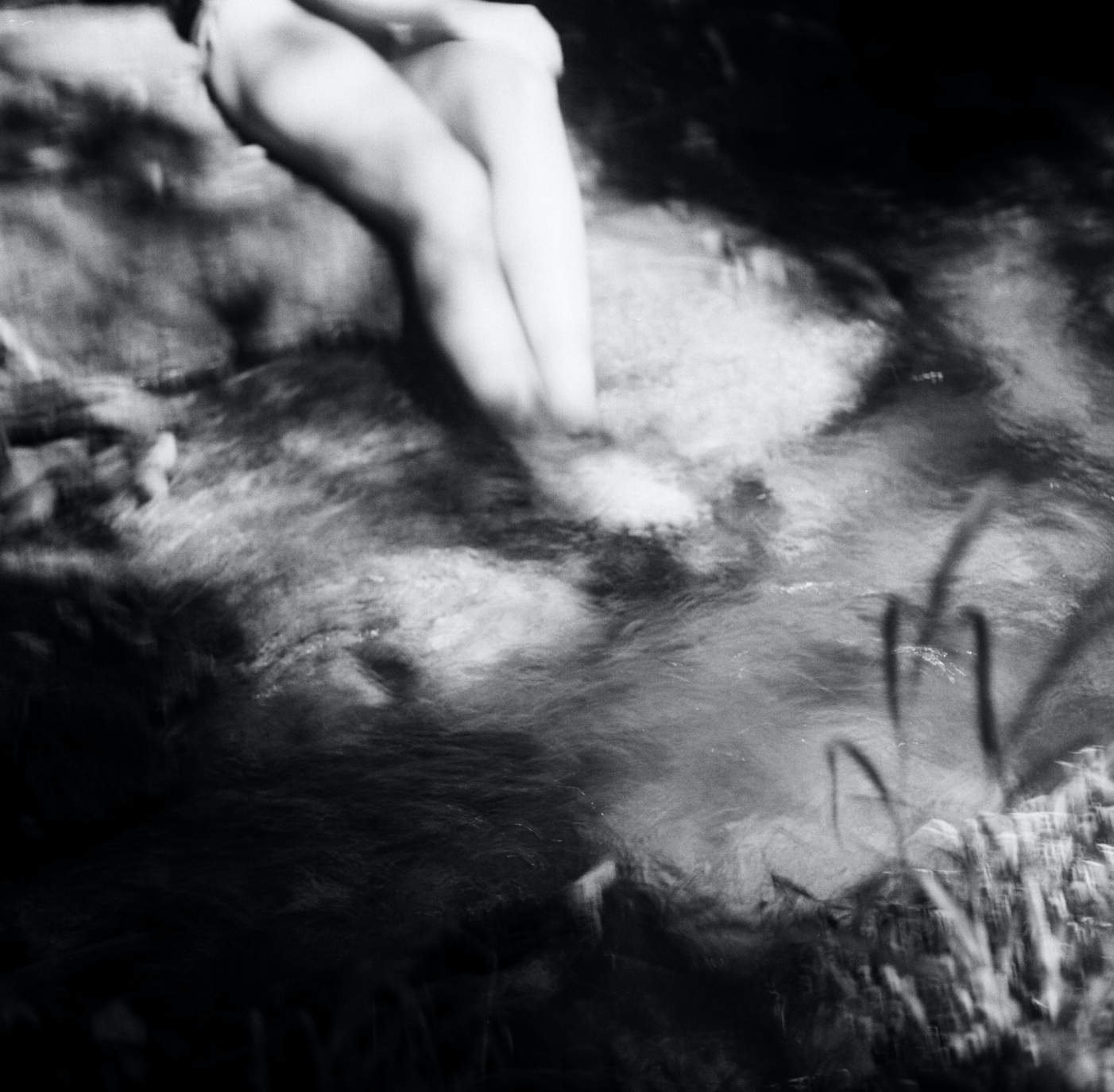 Black and white photo of a person's legs and feet in a creek or river, with water flowing around them.