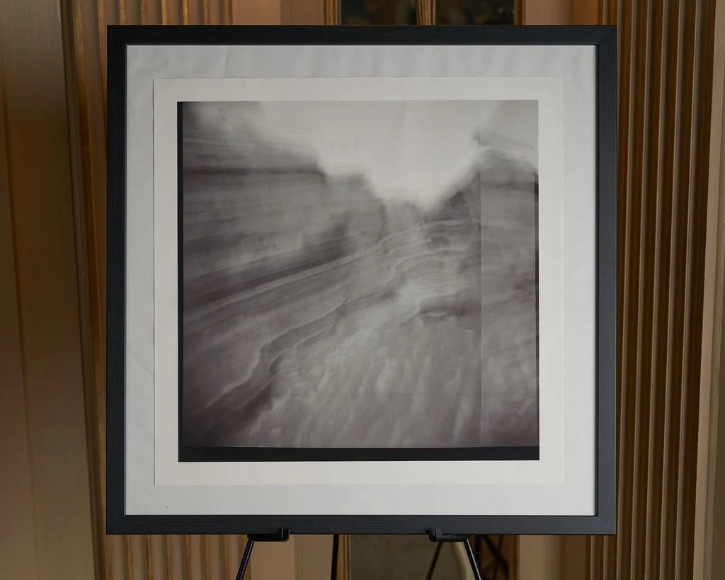 A blurry black and white photograph of a landscape with trees and water, displayed on an easel.