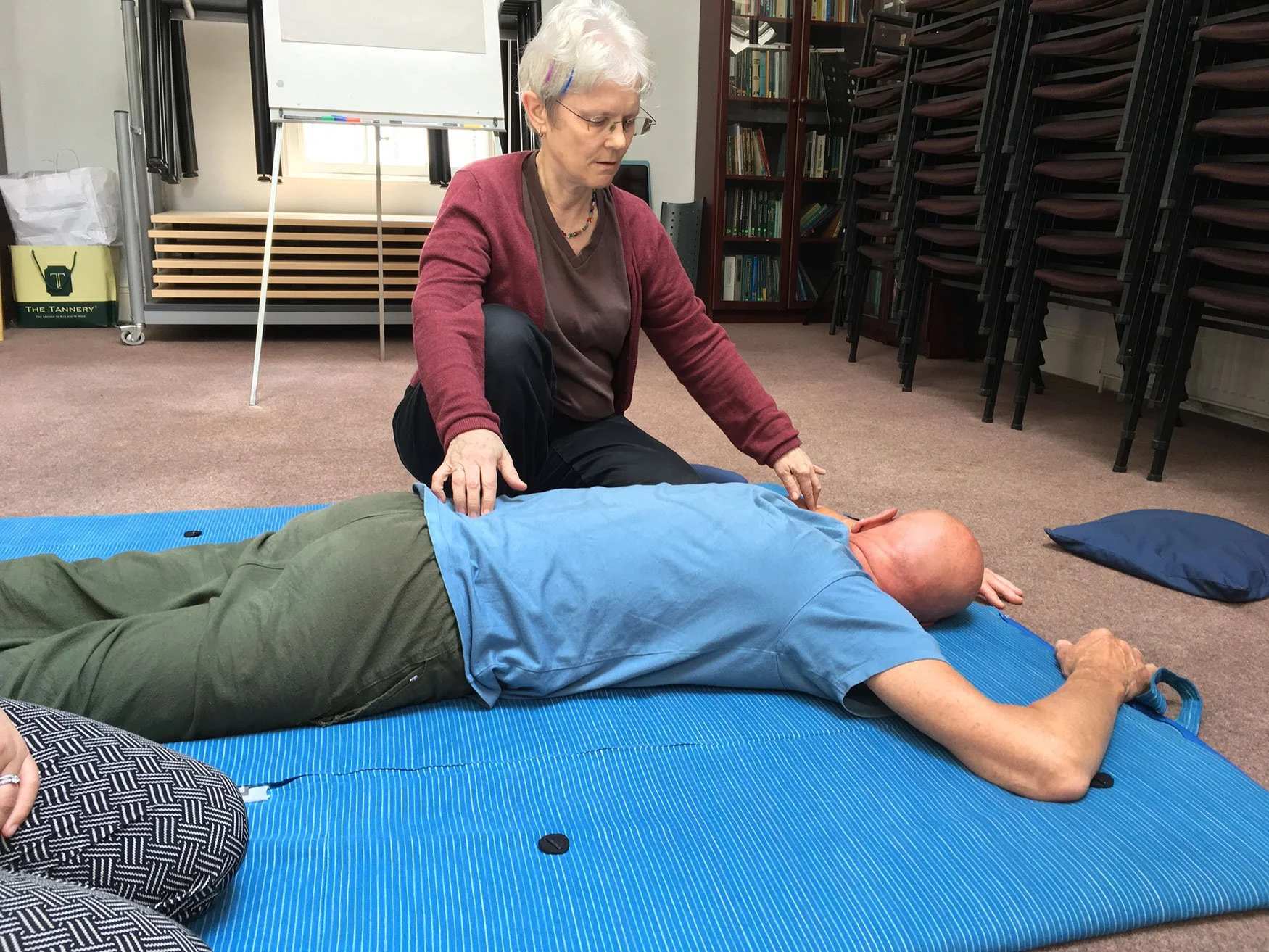 Veronica Howard demonstrating Shiatsu via points on the back and shoulder of a student who lies face down on a futon on the ground