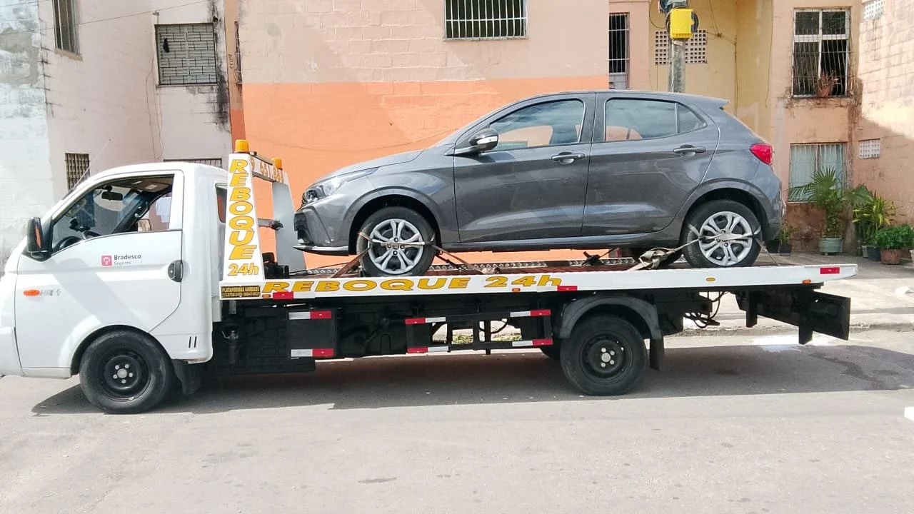 Carro cinza sendo transportado em um caminhão de rebocamento na rua