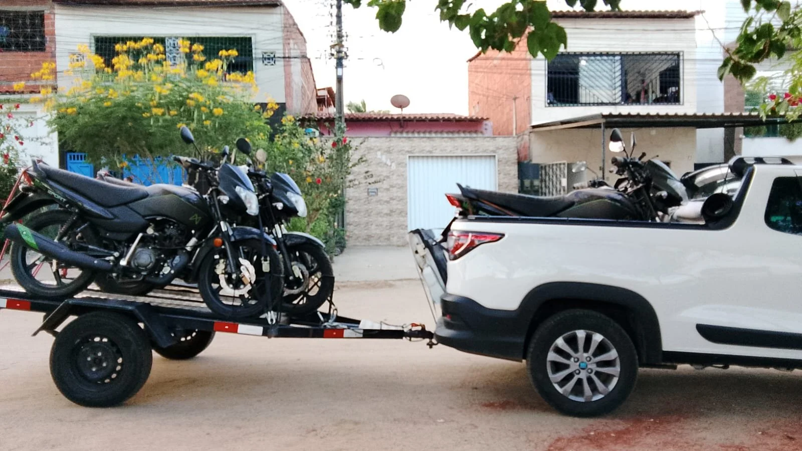 Carro branco transportando duas motos na cidade