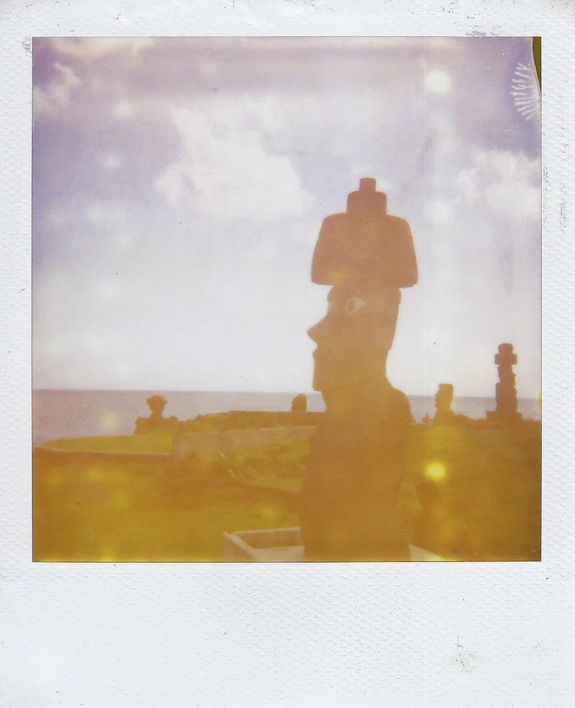Silhouette of a Moai statue on Easter Island, against a bright sky with clouds and a partly visible sun.