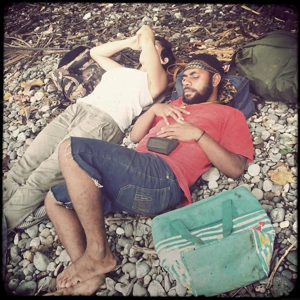 Two people sleeping on rocky ground on a beach in Papua New Guinea