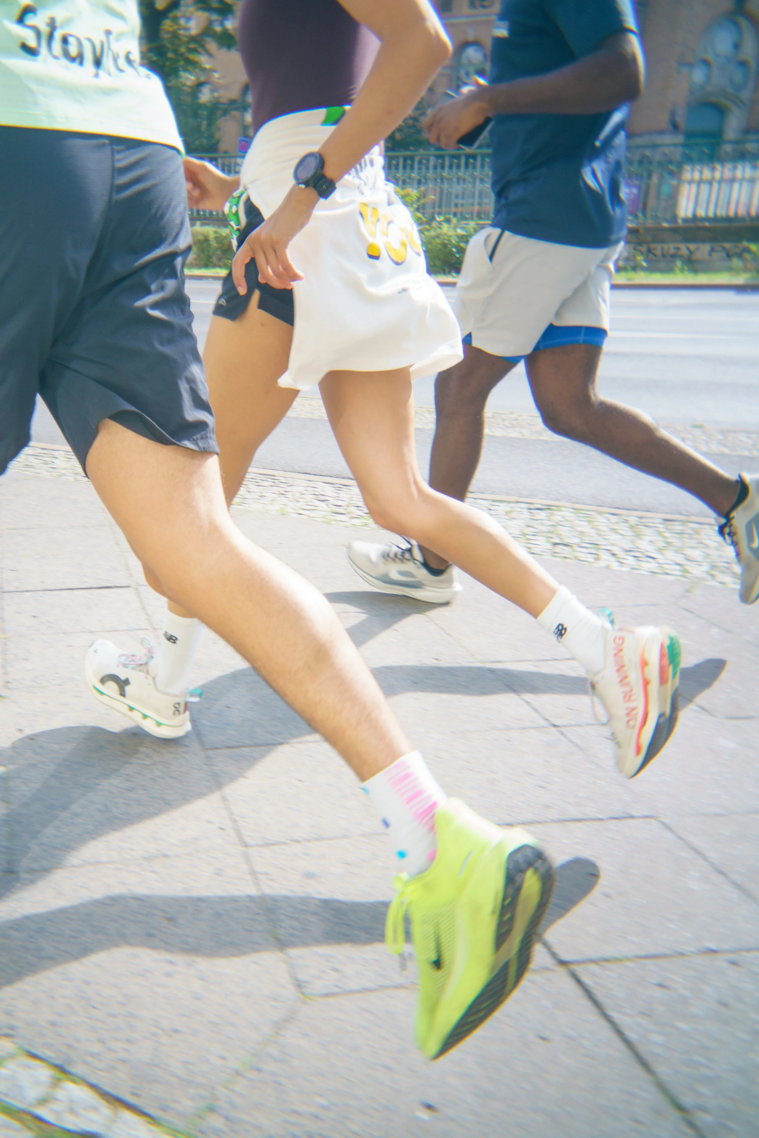 Three runners in athletic wear running on a city sidewalk, with a building and trees in the background.