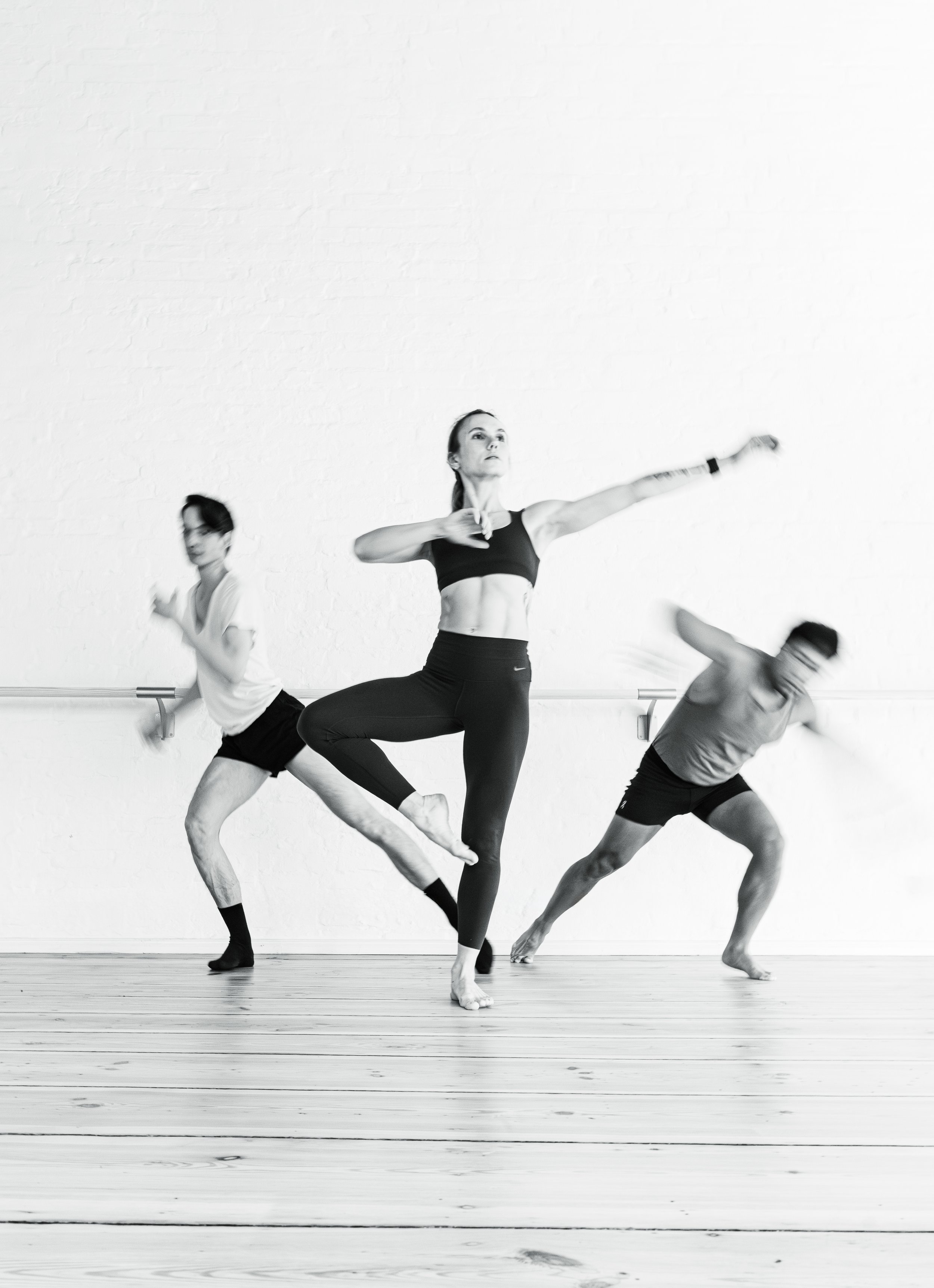 Three ballet dancers practicing in a studio, with the central dancer performing an arabesque pose.