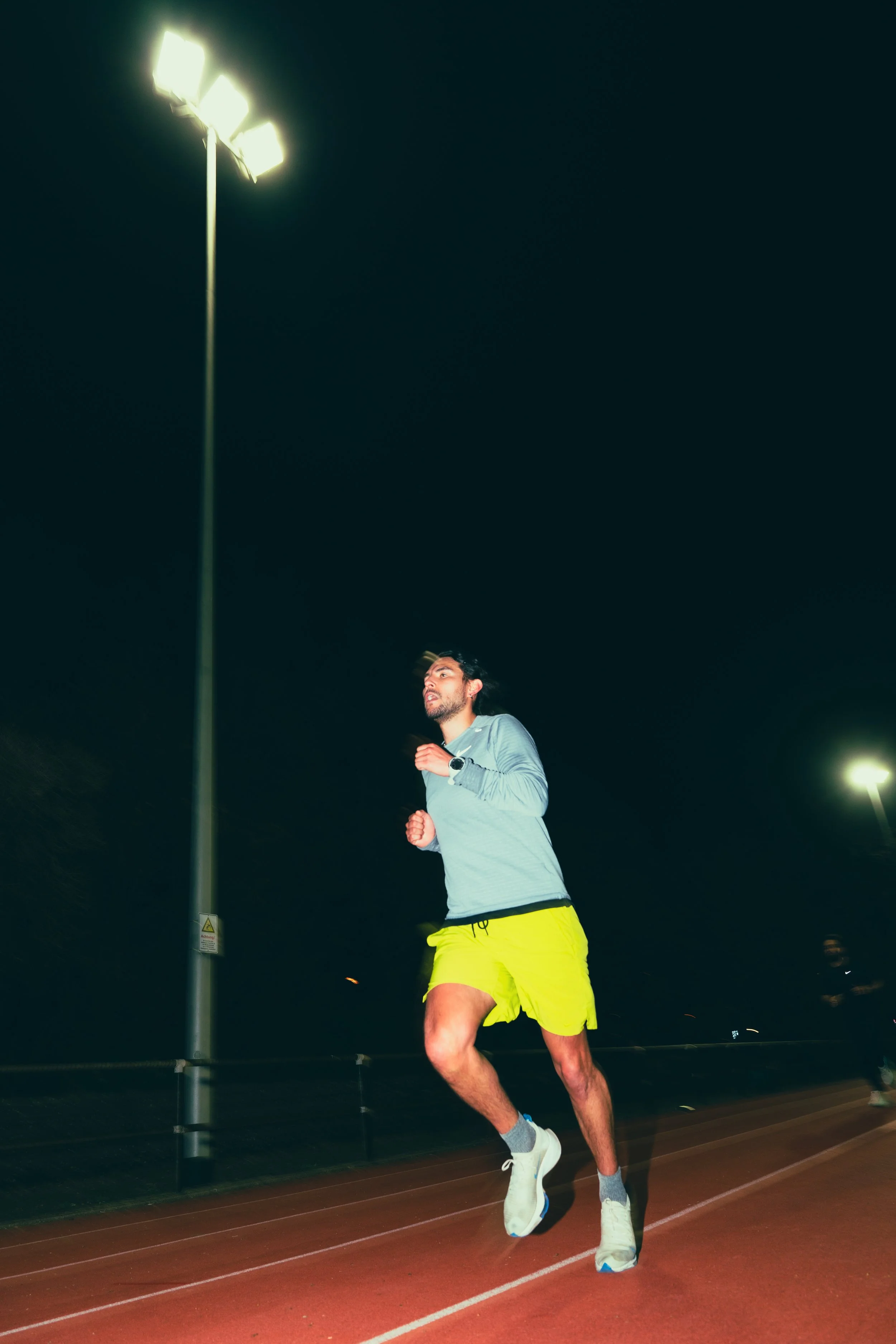 A man running on a track at night under artificial lights.