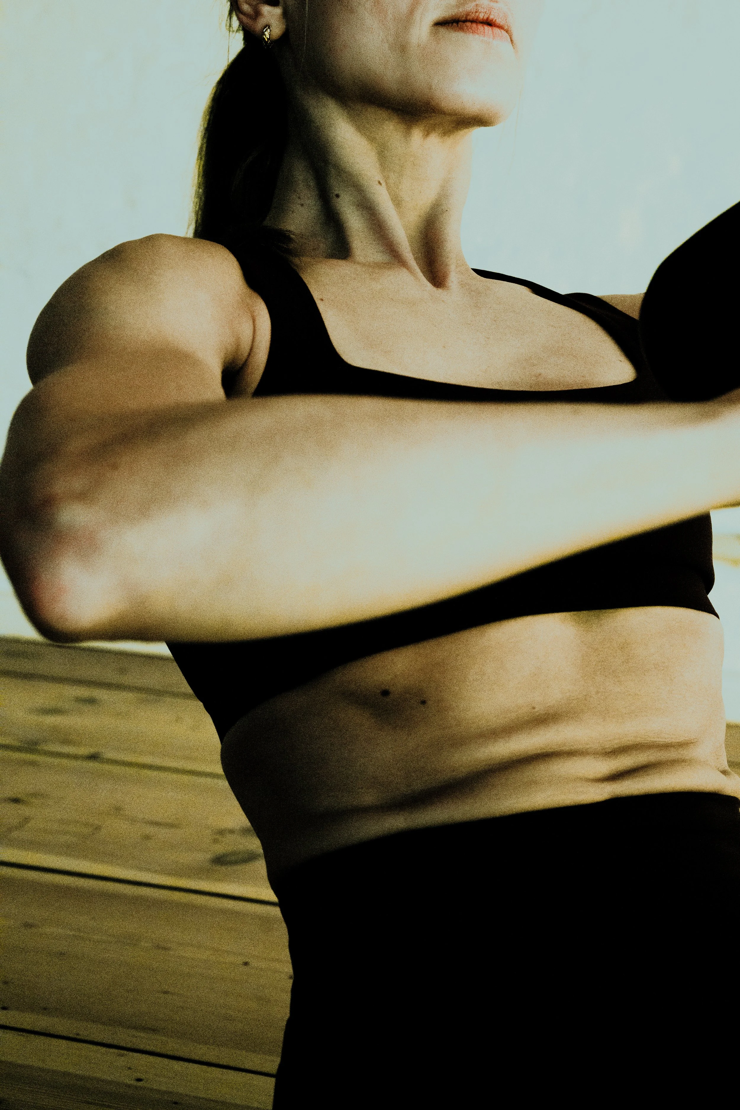 A woman exercising indoors, lifting a weight with her right arm, wearing a black sports bra and black leggings.