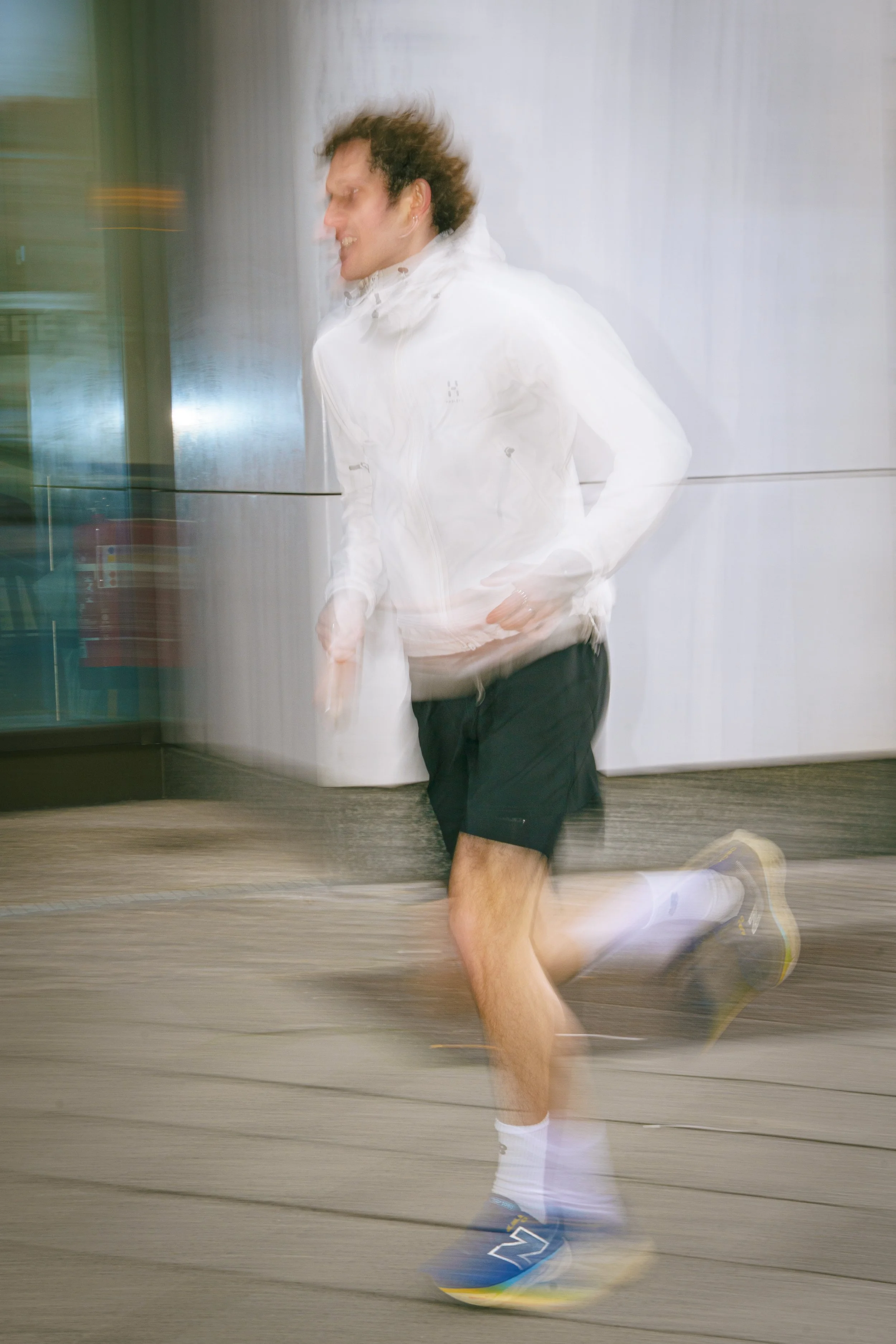 A man running outdoors in motion blur, wearing a white jacket, black shorts, white socks, and running shoes.