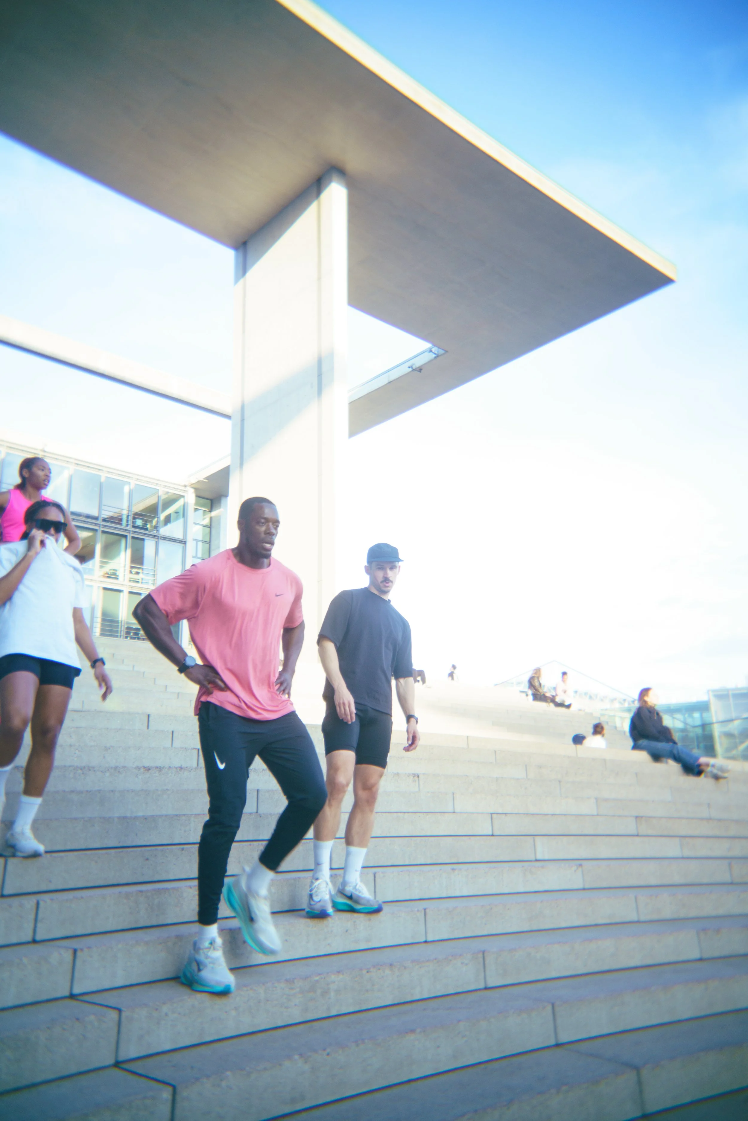 People walking down concrete stairs outside near modern glass building under a blue sky.