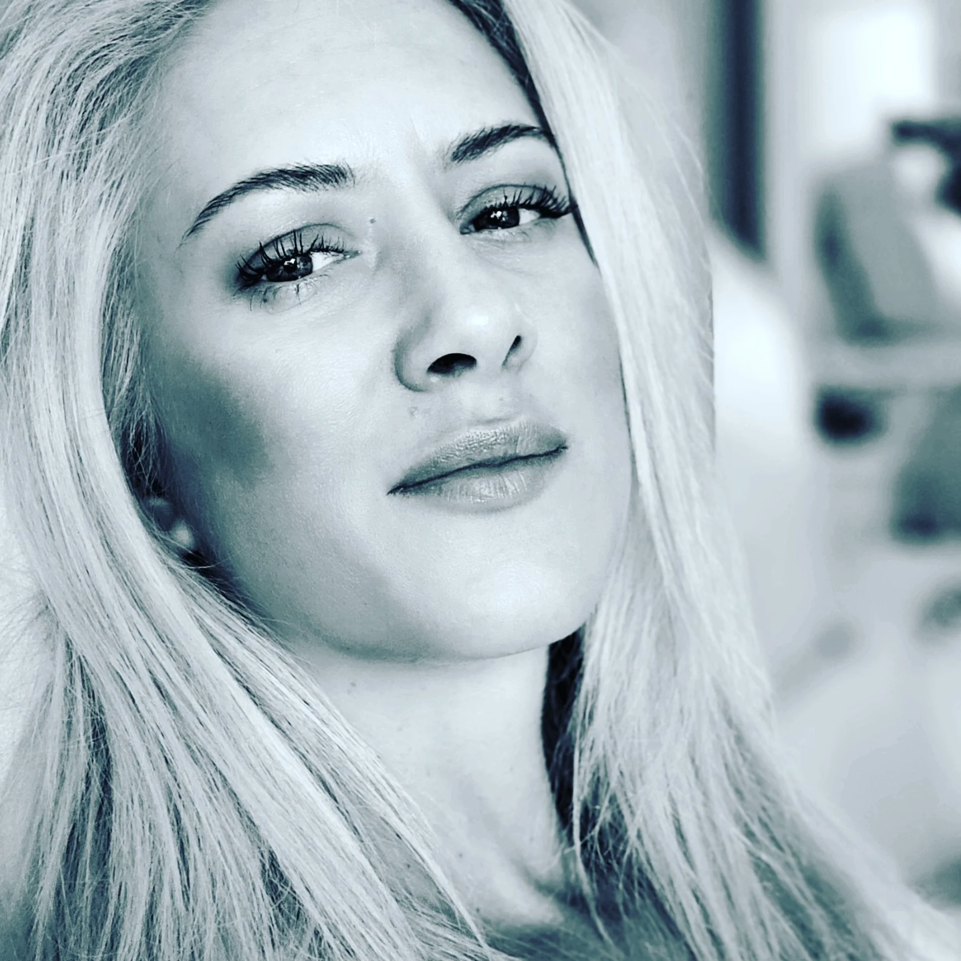 A close-up black-and-white portrait of a woman with long, straight blonde hair, looking confidently at the camera.