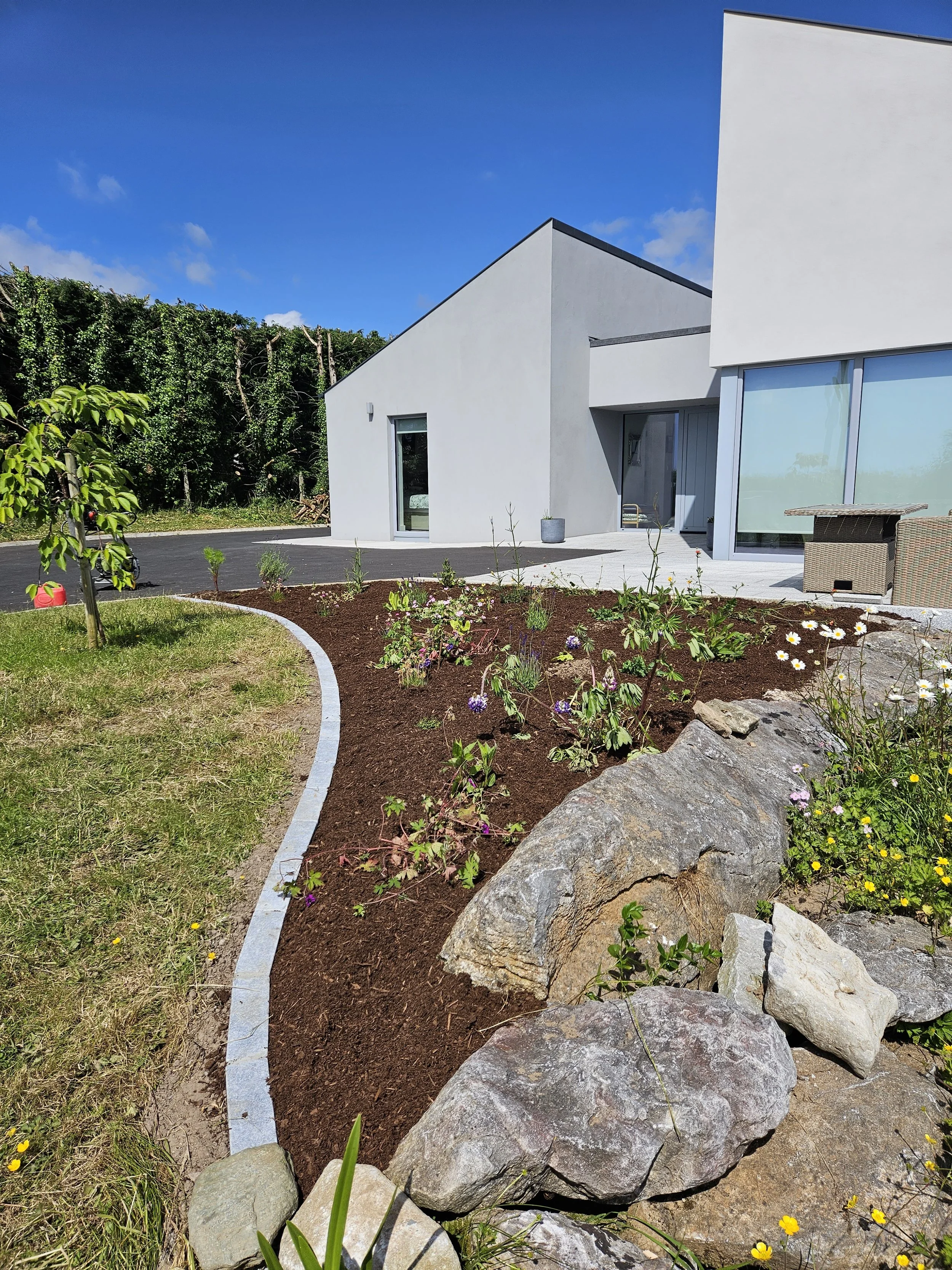 Modern white house with landscaped garden and flower bed with rocks under a blue sky.
