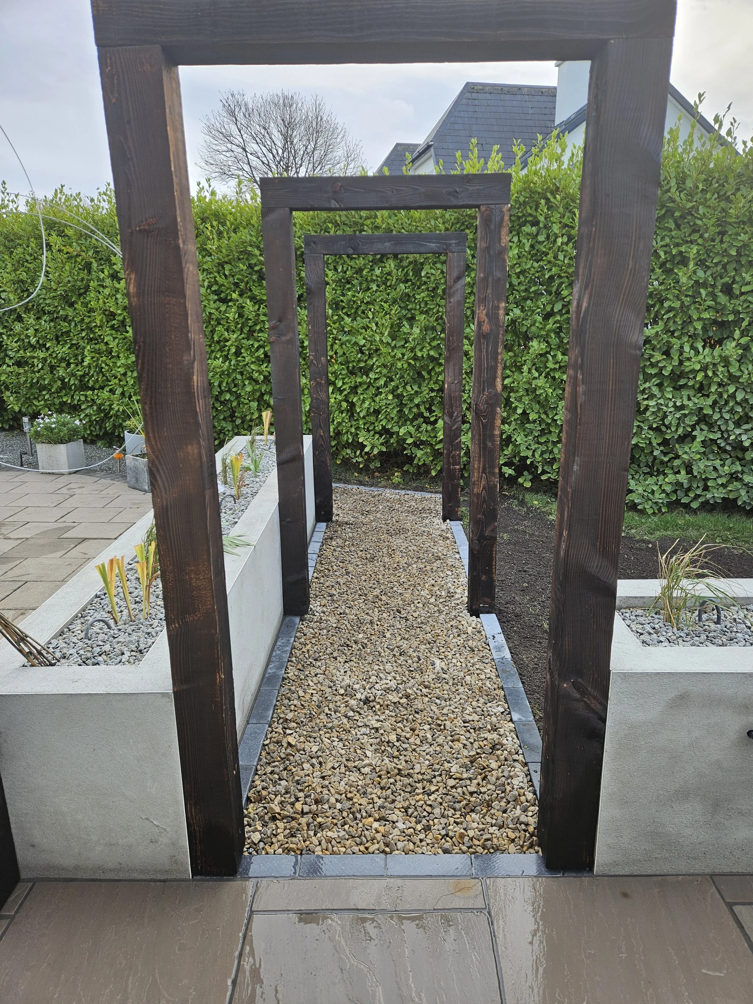 Garden pathway with wooden arches, gravel walkway, and surrounding greenery.