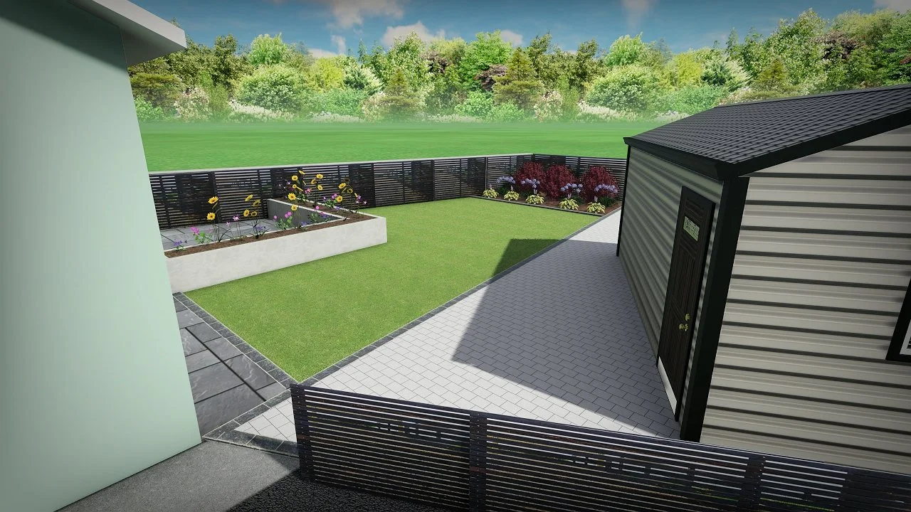 View of a backyard with a green lawn, flower bed, flower plants, a paved patio, fenced yard, and trees in the background.