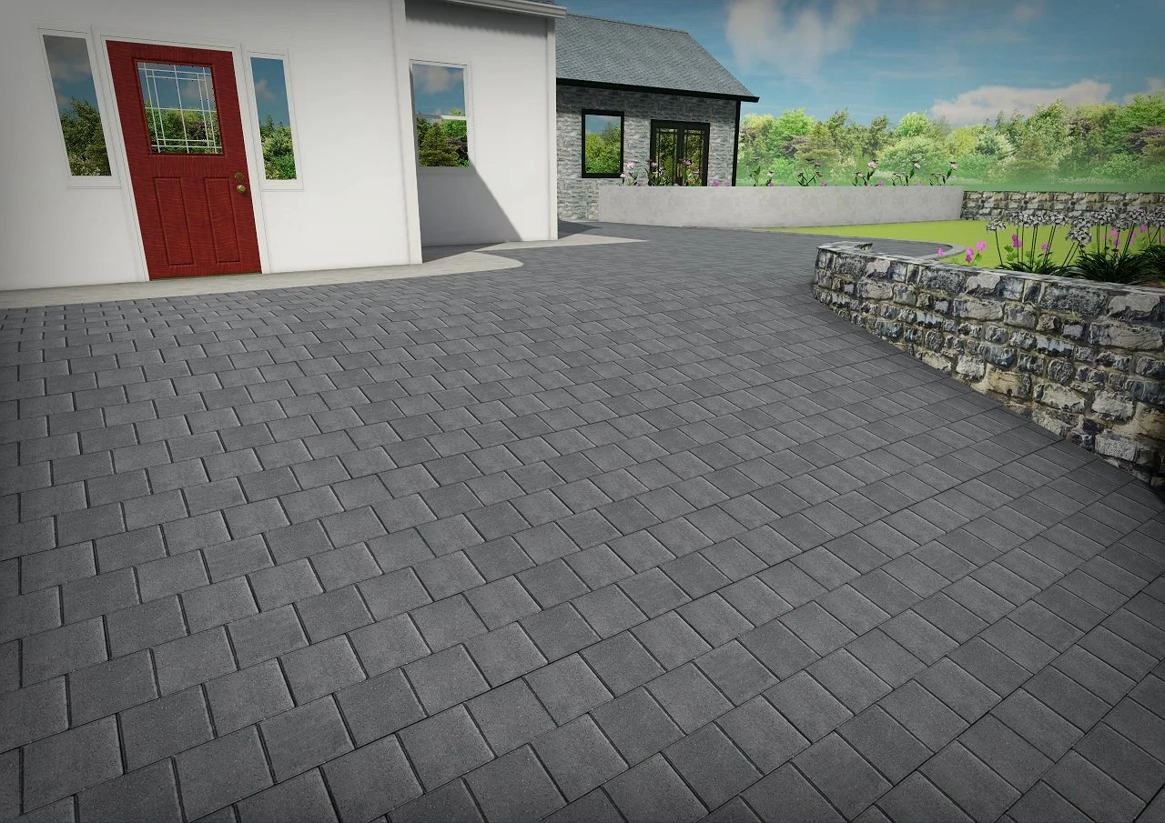 A paved stone driveway leading to a white house with a red front door and multiple windows. There is a second building with a gray exterior and black window frames in the background. A garden area with pink flowers and a stone wall border can also be