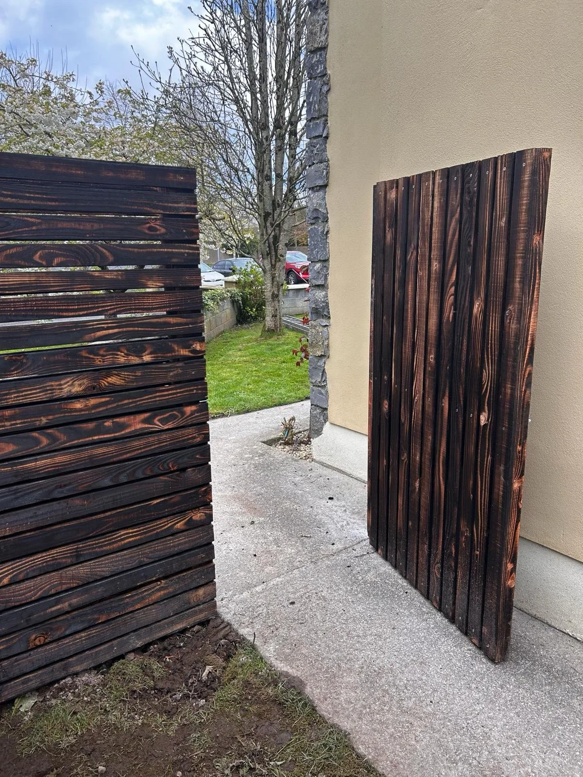 Wooden privacy fences on either side of a sidewalk leading to a backyard with grass and trees.