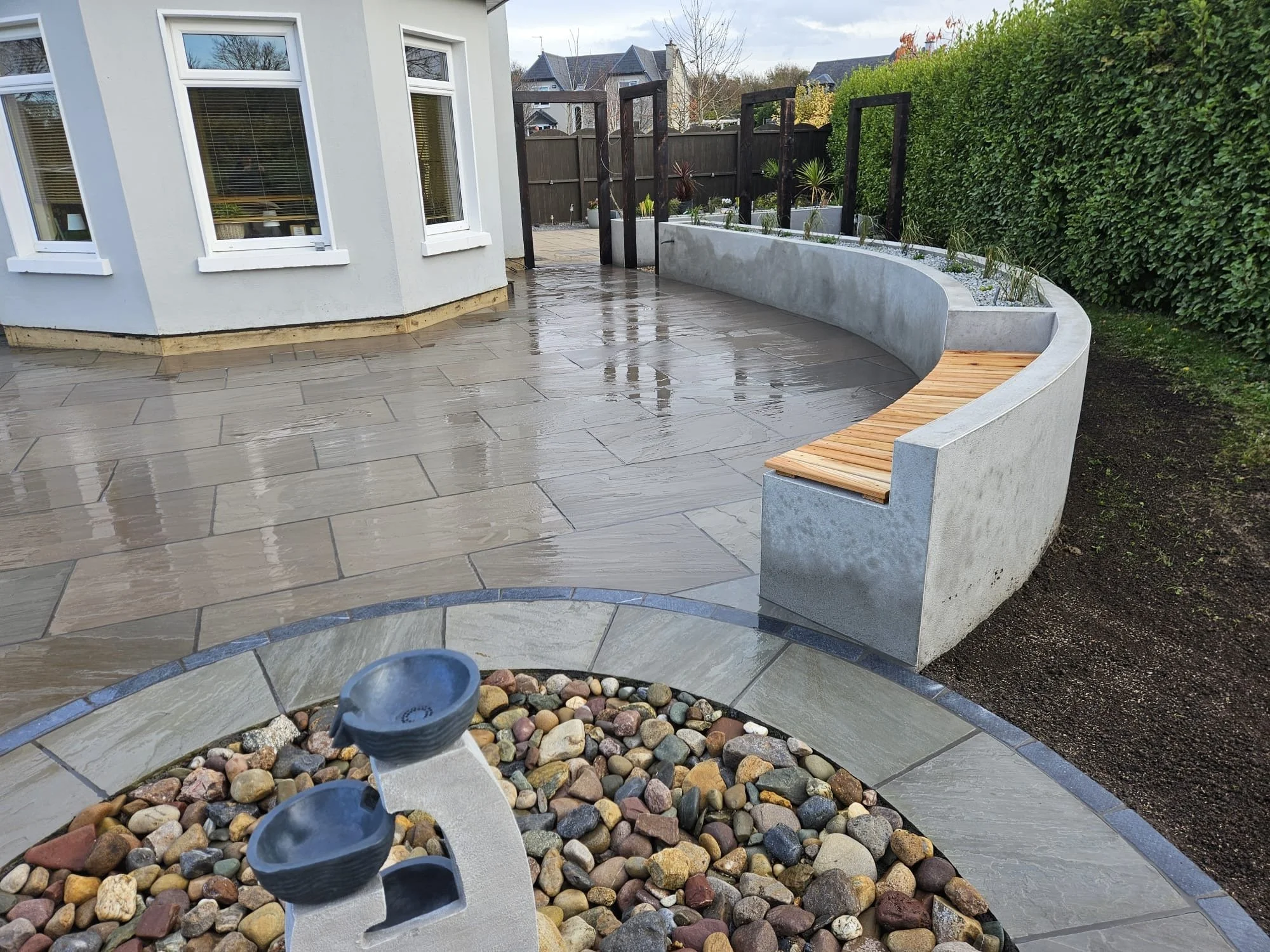 curved raised planters with feature cedar clad benches and water feature. natural stone paving and flamed Douglas fir arches