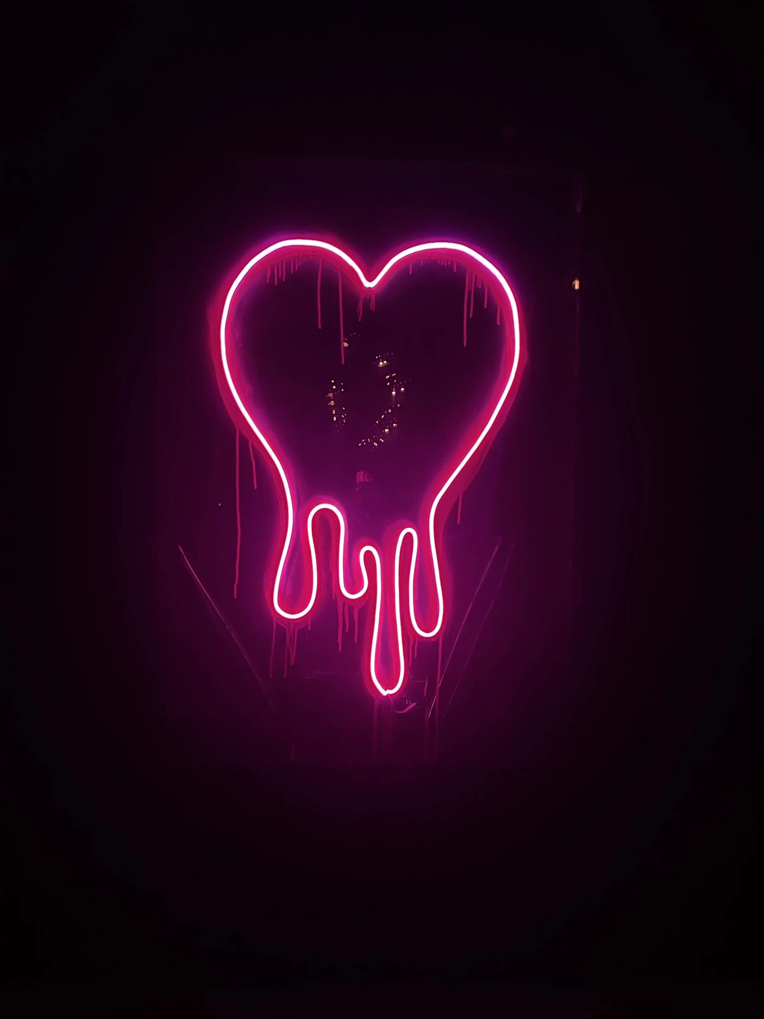 Pink neon light in the shape of a melting heart against a dark background.