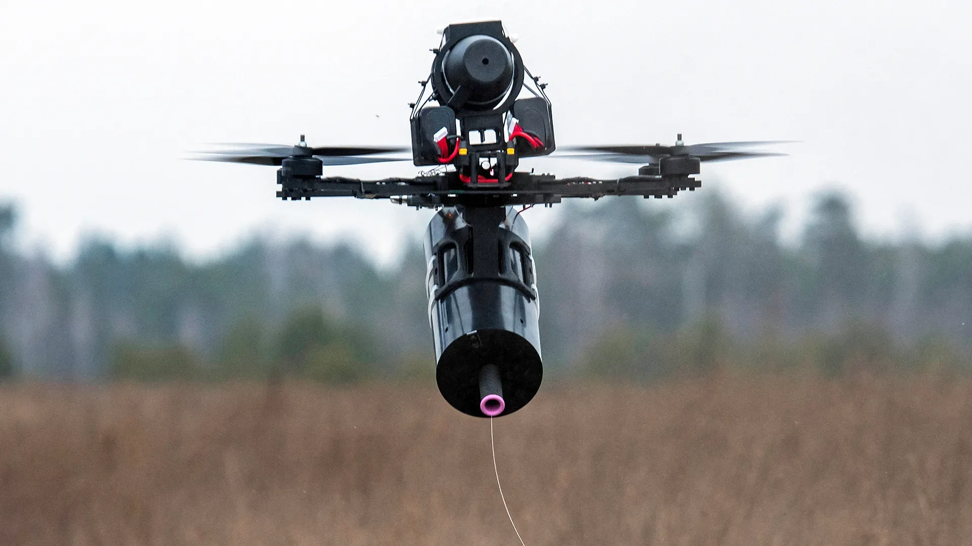 A drone with a camera mounted underneath flying over a field.