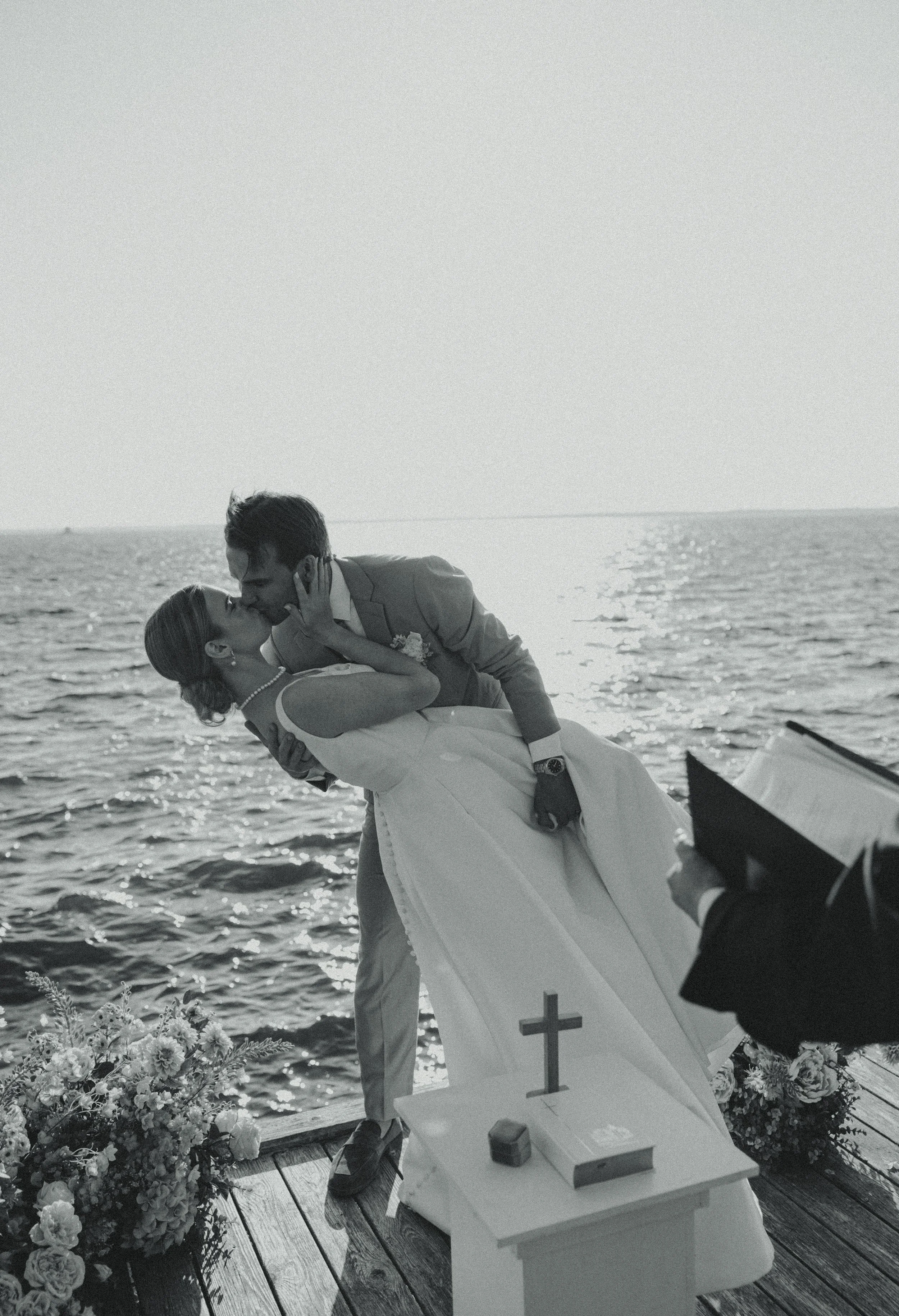 A couple getting married on a dock by the water, with the groom dipping the bride for a kiss.