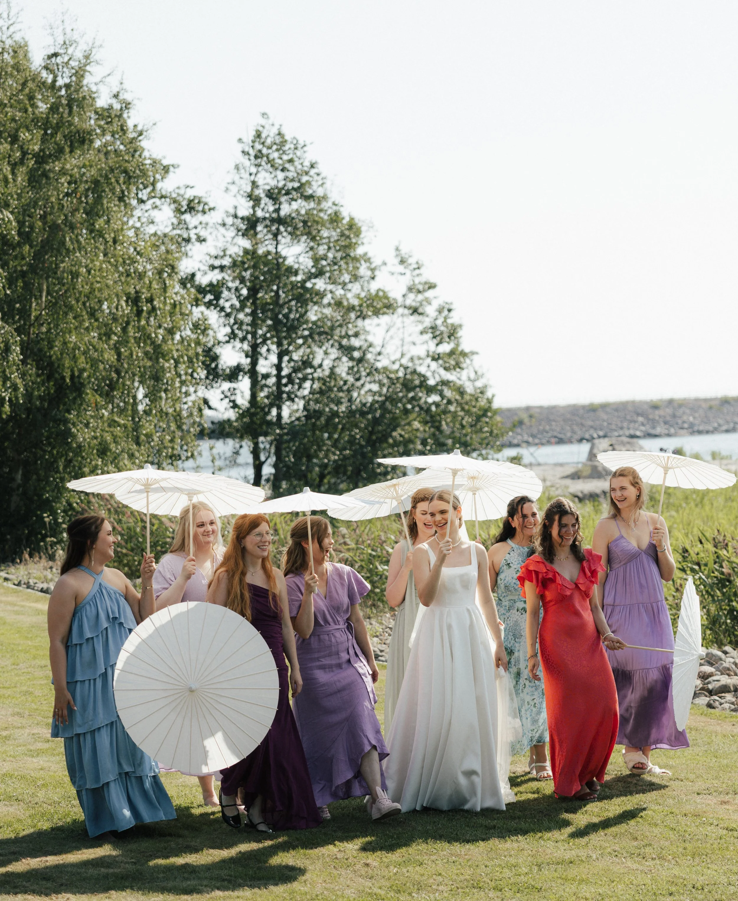 A group of women in colorful dresses holding white umbrellas, walking outdoors on a sunny day.