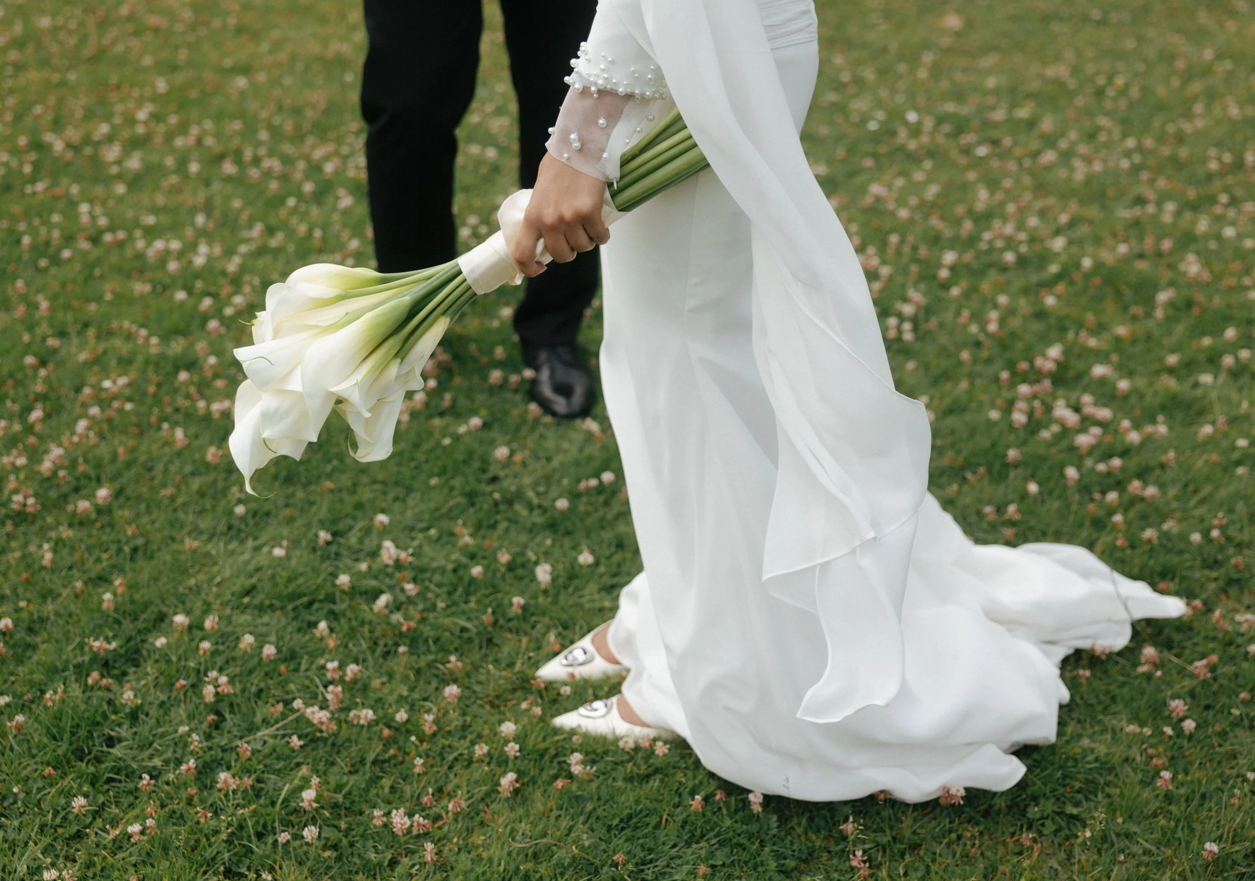 A bride in a white wedding dress holding a bouquet of calla lilies on a grassy field.