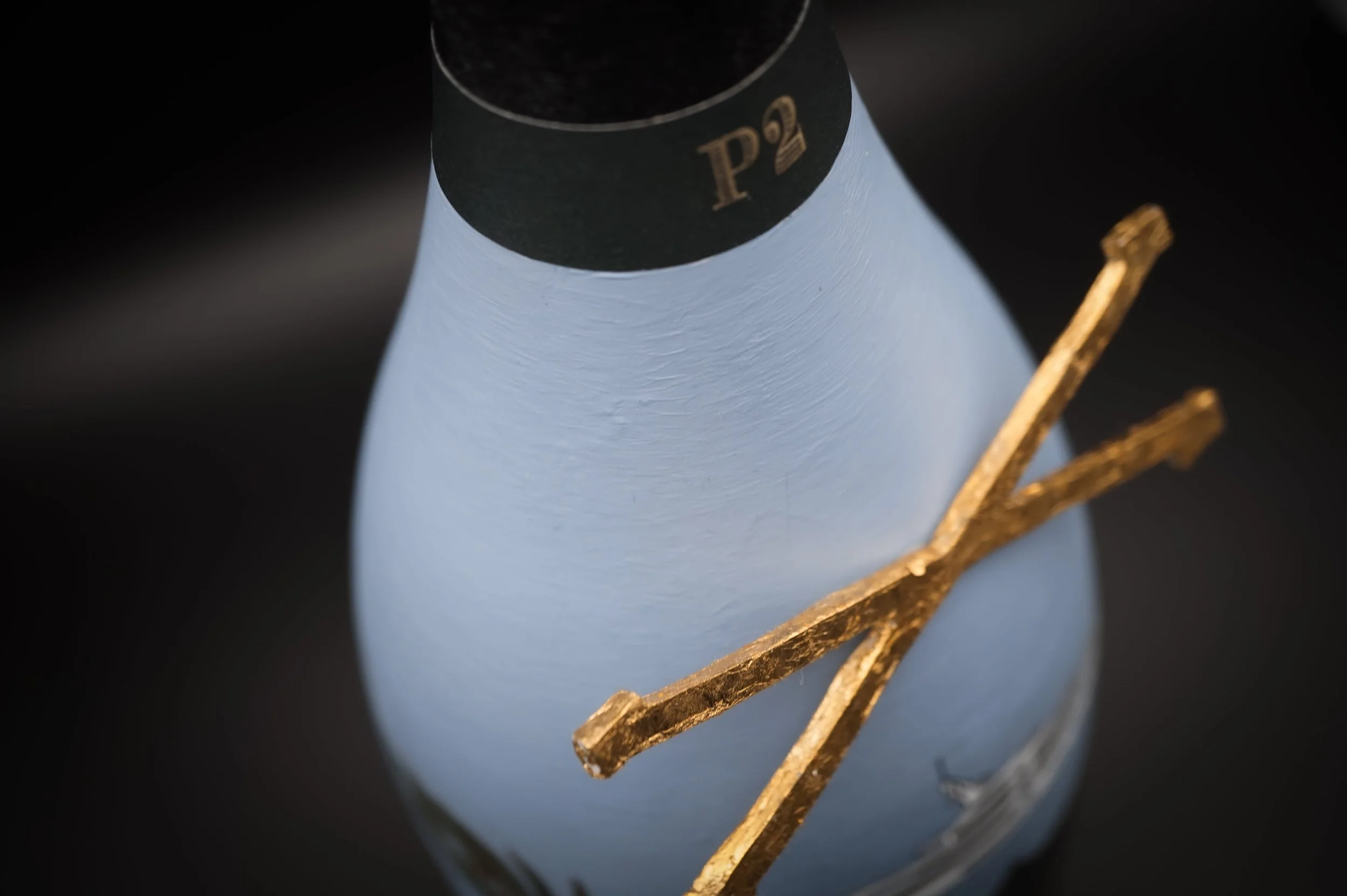 Macro close-up of hand-painted Dom Pérignon P2 bottle showing visible brushstroke texture on blue paint and gold leaf cross detail