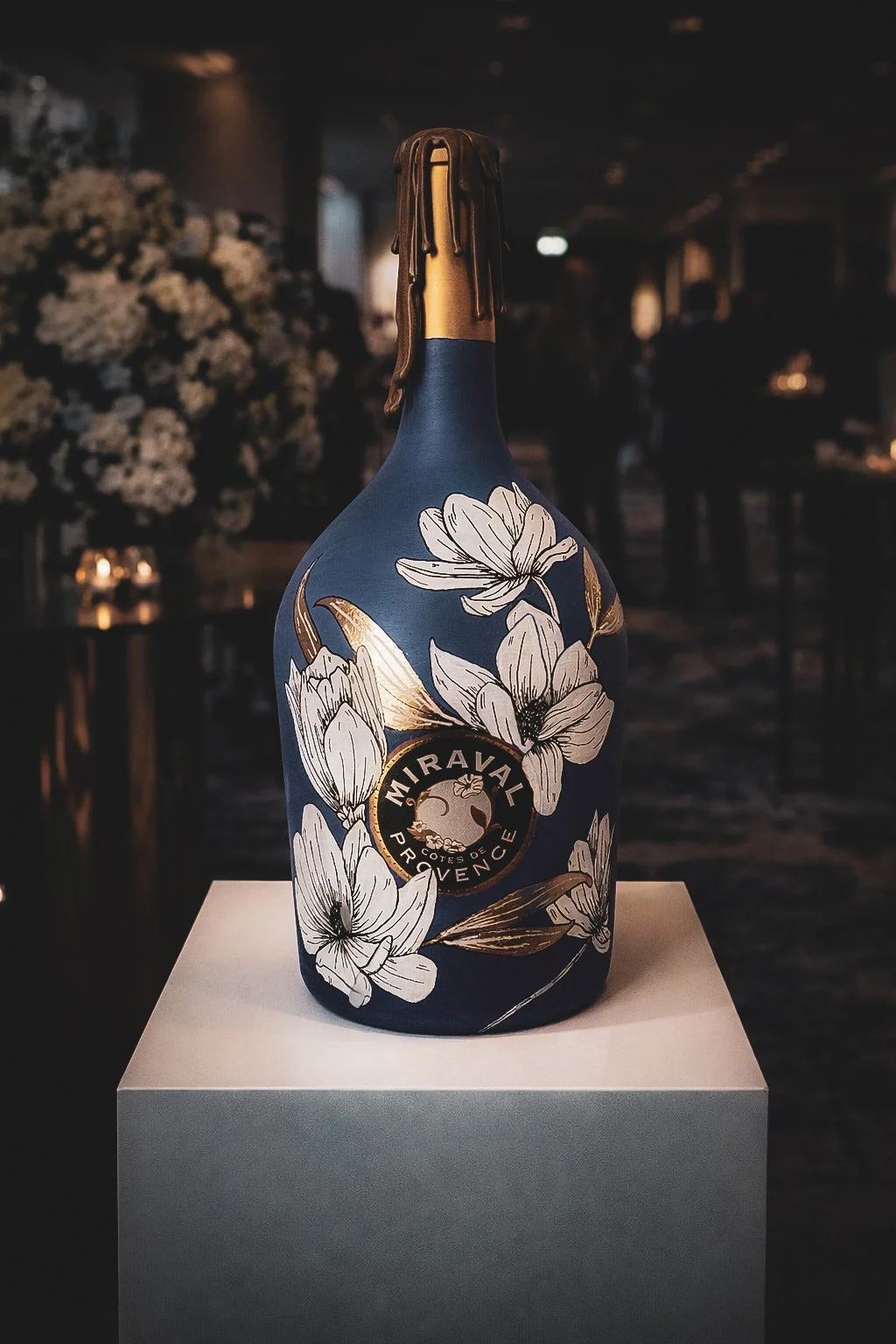 Hand-painted Miraval bottle with white floral and gold detail displayed at a luxury event