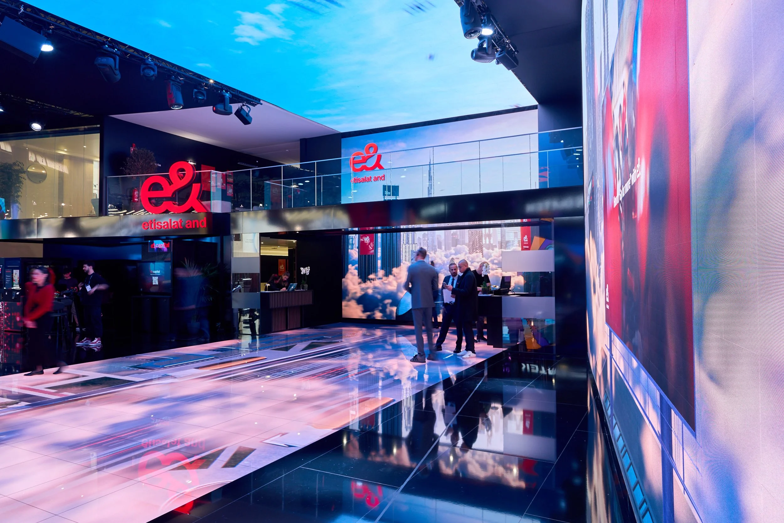 Inside a modern corporate event or conference featuring a large digital display, attendees in business attire, and prominent "etisalat and" signage and logos.