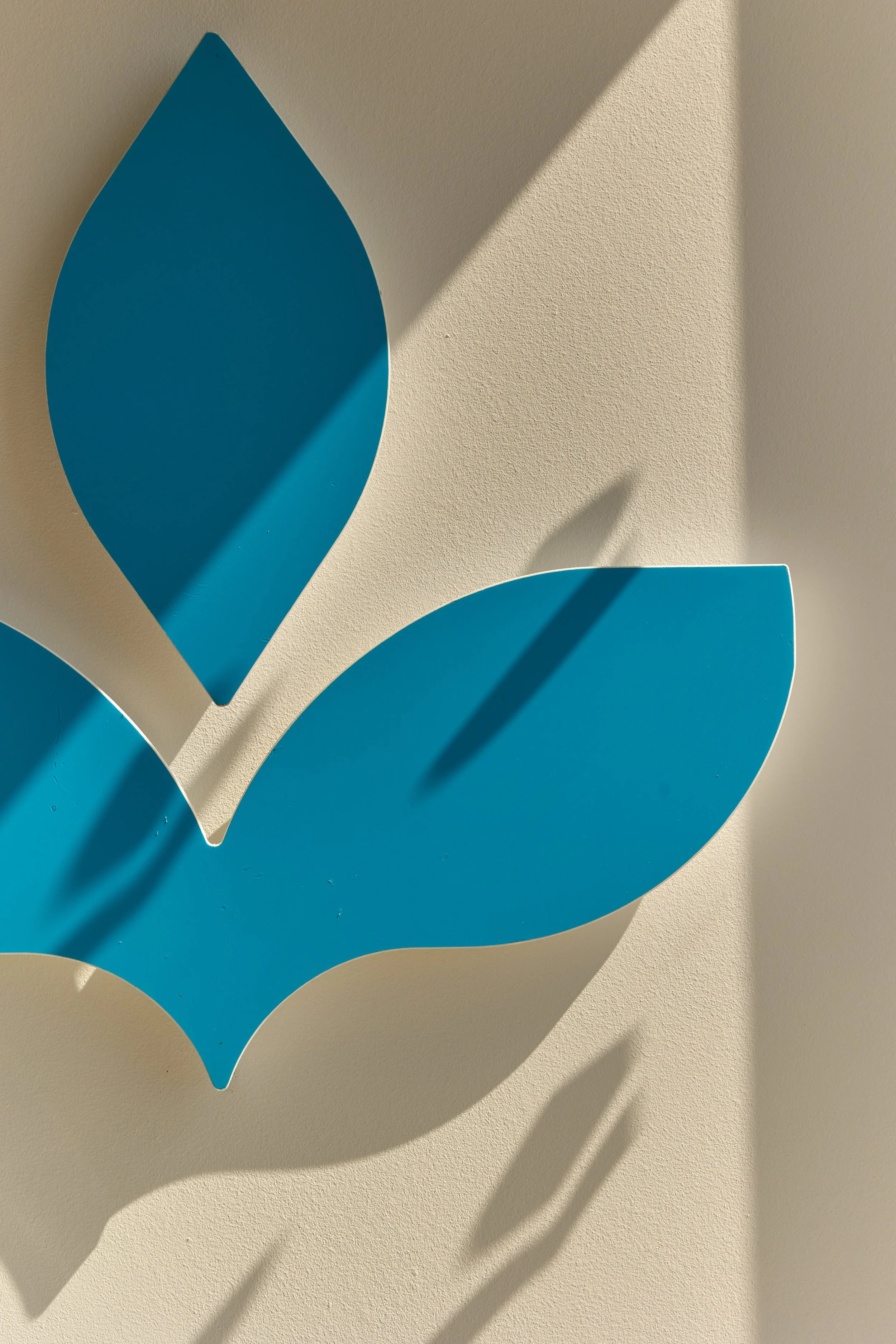 Close-up of a modern blue wall decoration with leaf shapes casting shadows on a beige wall.