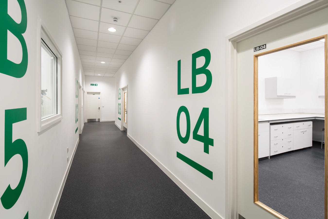 Science Creates St. Philip's laboratory corridor. A Deep Tech incubator with containment level 2 laboratories, and a warehouse to lab conversion.  White walls, grey vinyl, ceiling with lights, and room doors labelled LB 04, LB 03, and LB 05.