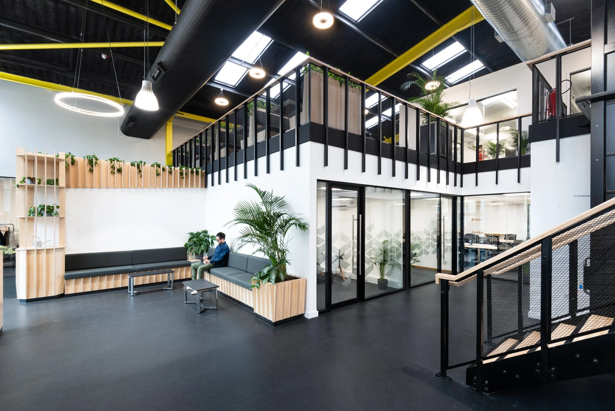 Science Creates Old Market atrium space - modern Deep Tech Incubator, with containment level 2 laboratories, and a warehouse to lab conversion.  Black flooring, green plants, and asitting area with black and wooden furniture.