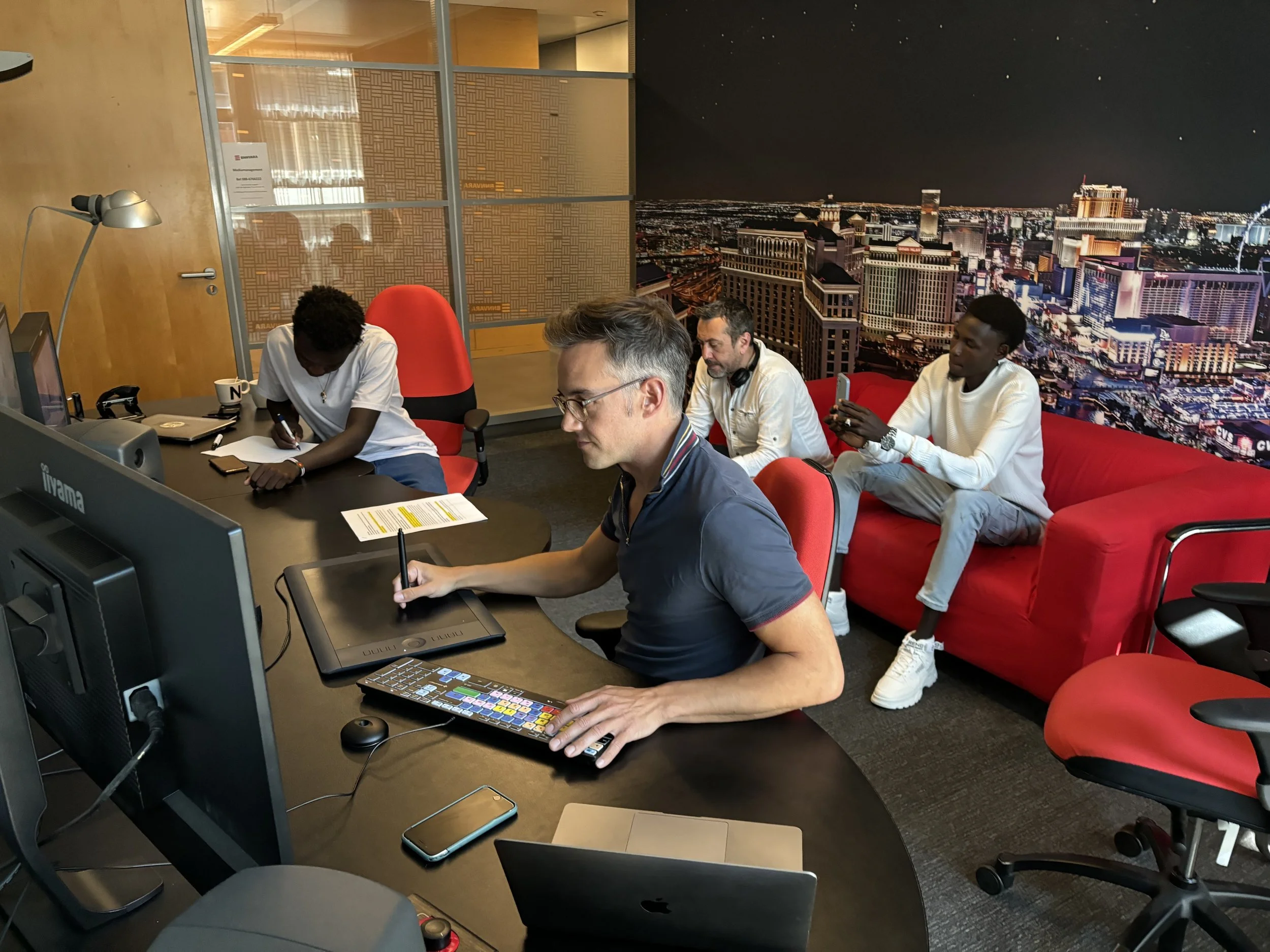 A group of four men working in an office with a cityscape mural on the wall behind them, some using tablets and smartphones.
