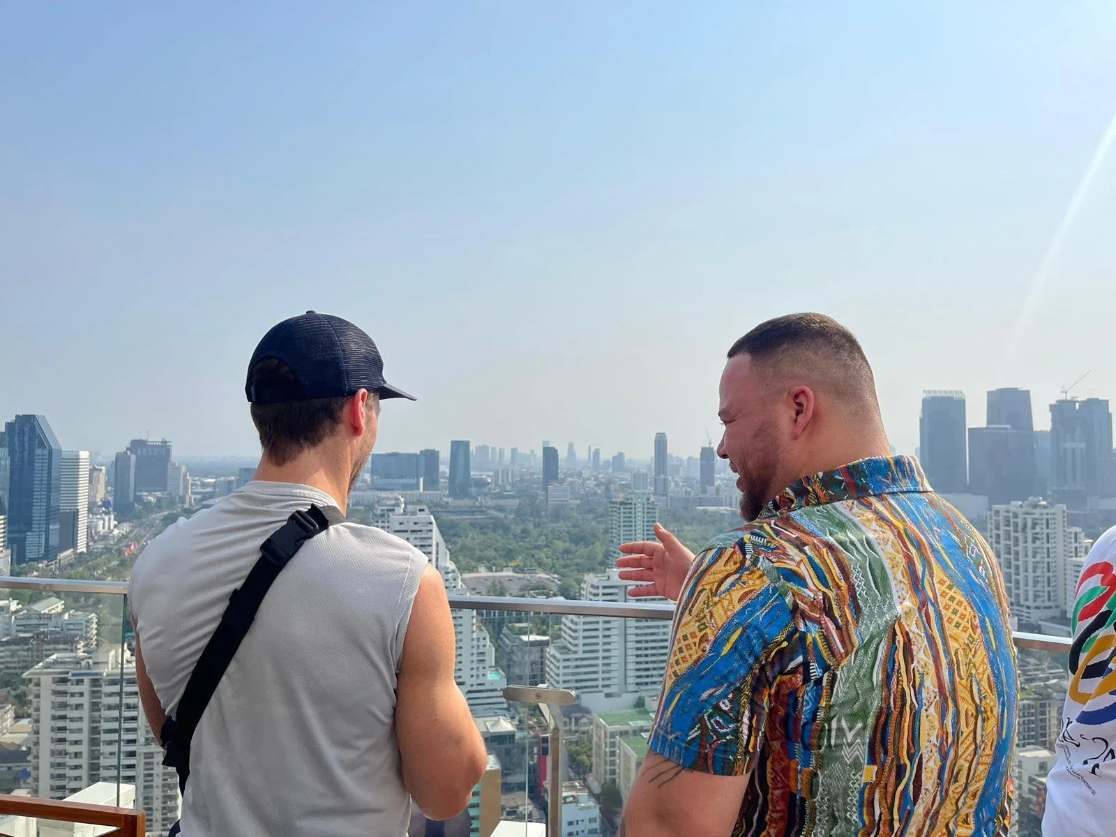 Two men standing on a rooftop overlooking a city skyline, engaging in conversation.