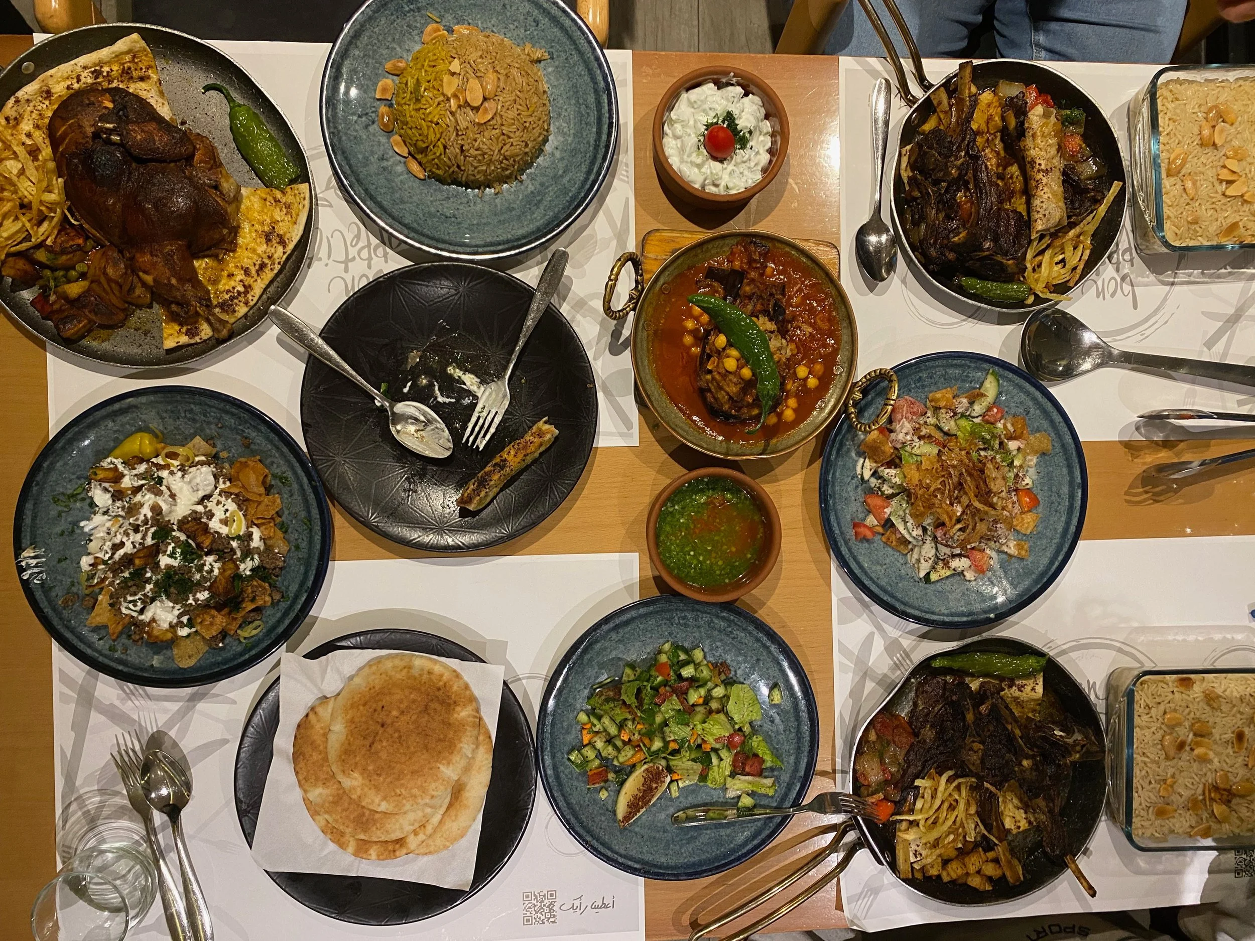 A variety of Middle Eastern dishes on a table, including rice dishes, salads, flatbread, grilled meats, and desserts.